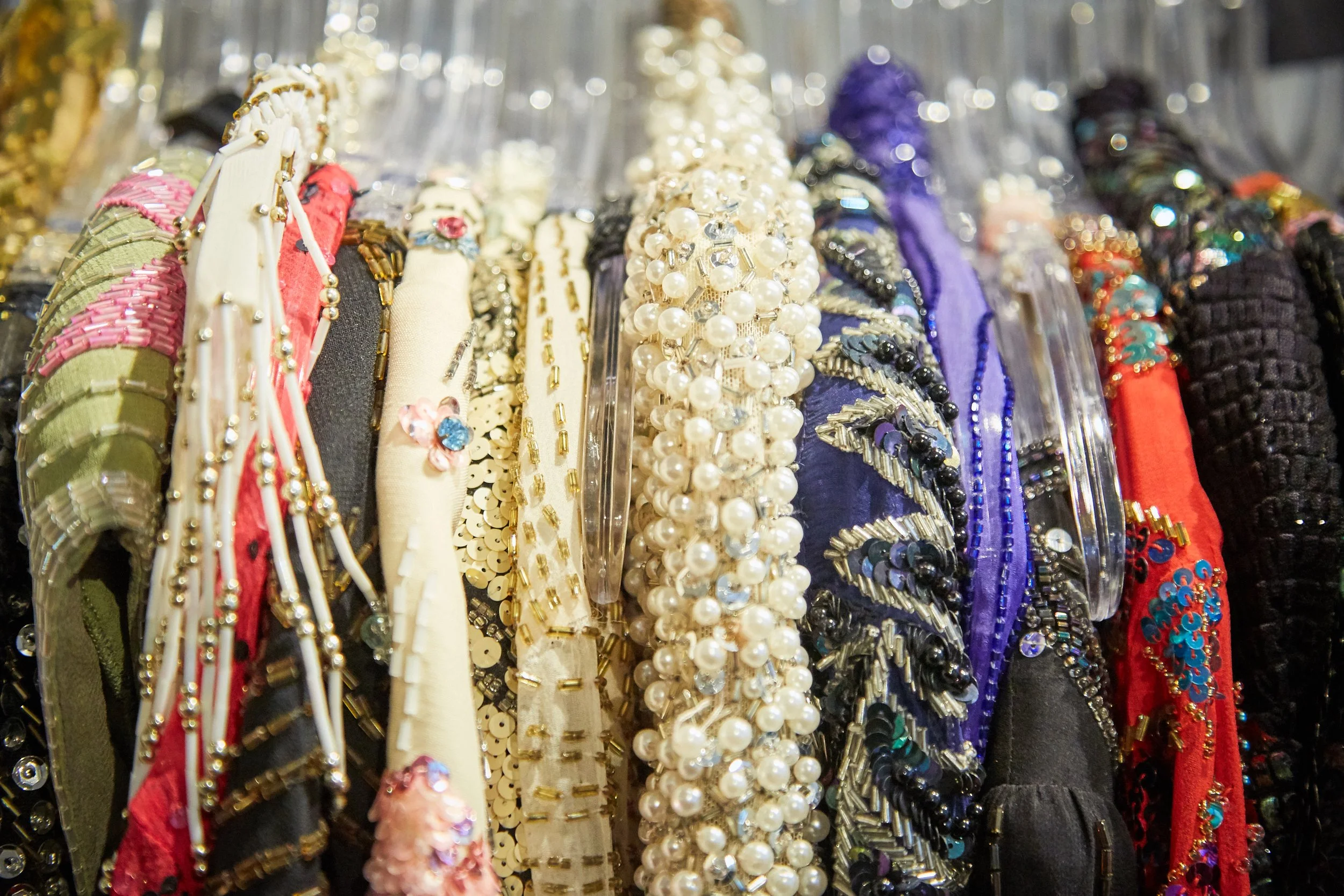 Close-up of various colorful beaded and embellished fabric headbands hanging on a rack.