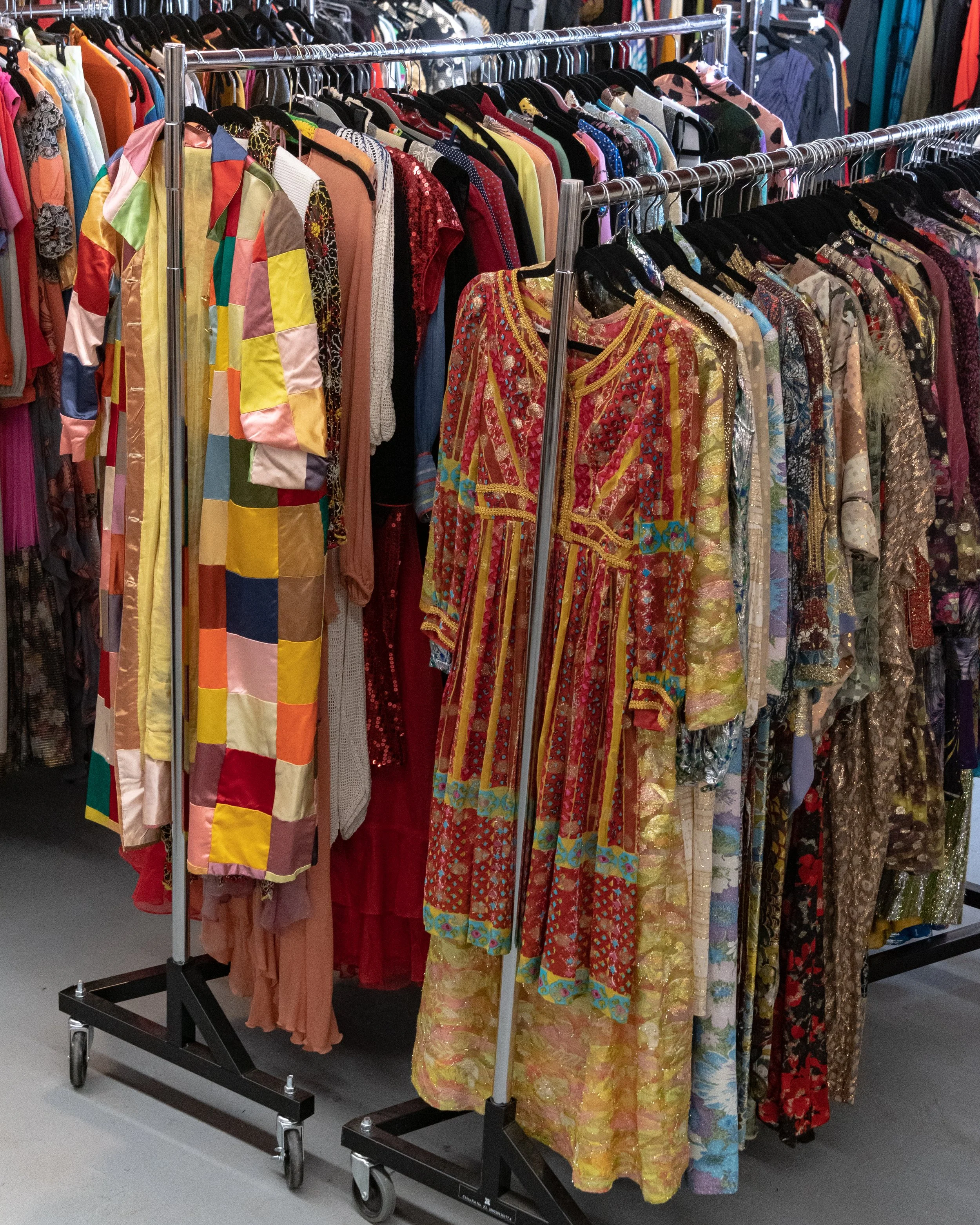 Clothing racks with colorful and patterned dresses and garments hanging in a store or thrift shop.