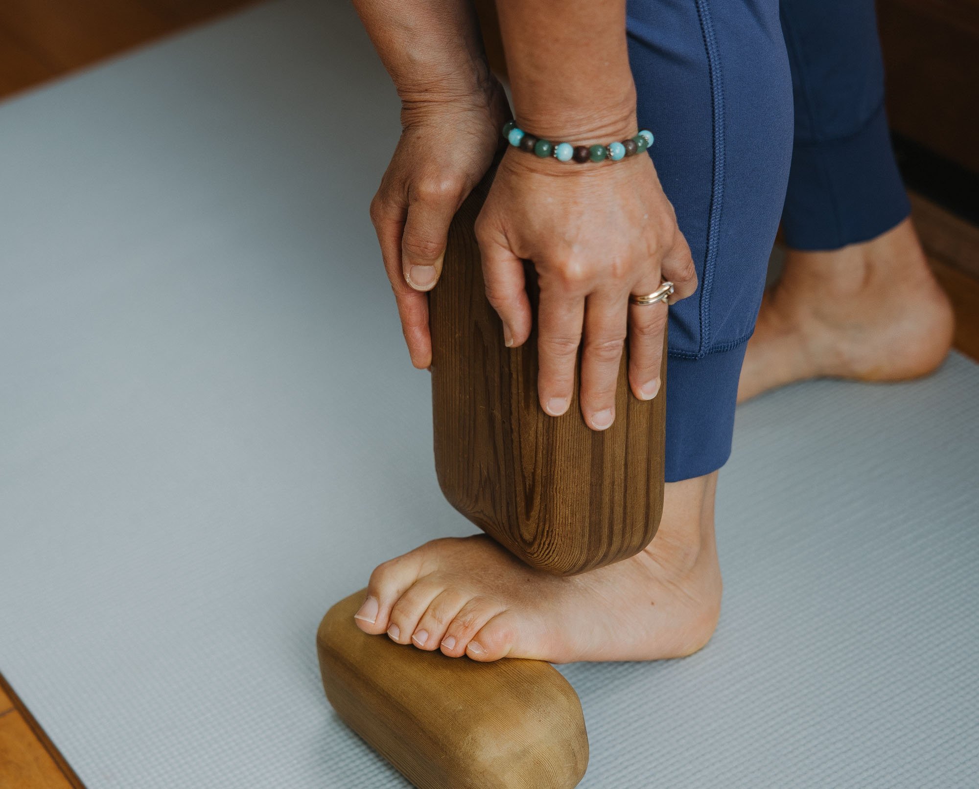 Close-up of a woman positioning a wood Block Therapy tool against her foot and lower leg for fascia release.