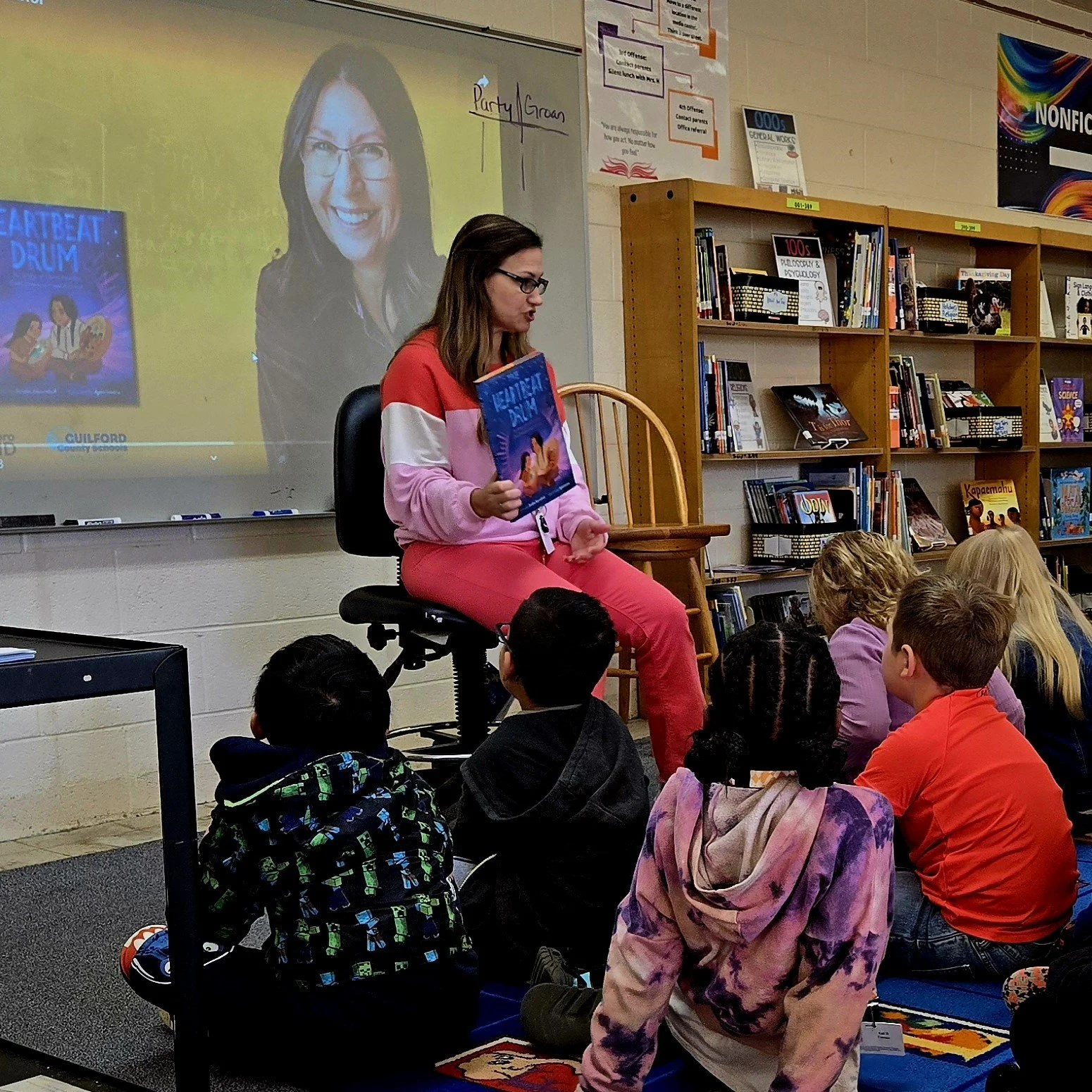 a photo of children listening to their teacher before they hear from a children's author virtually.