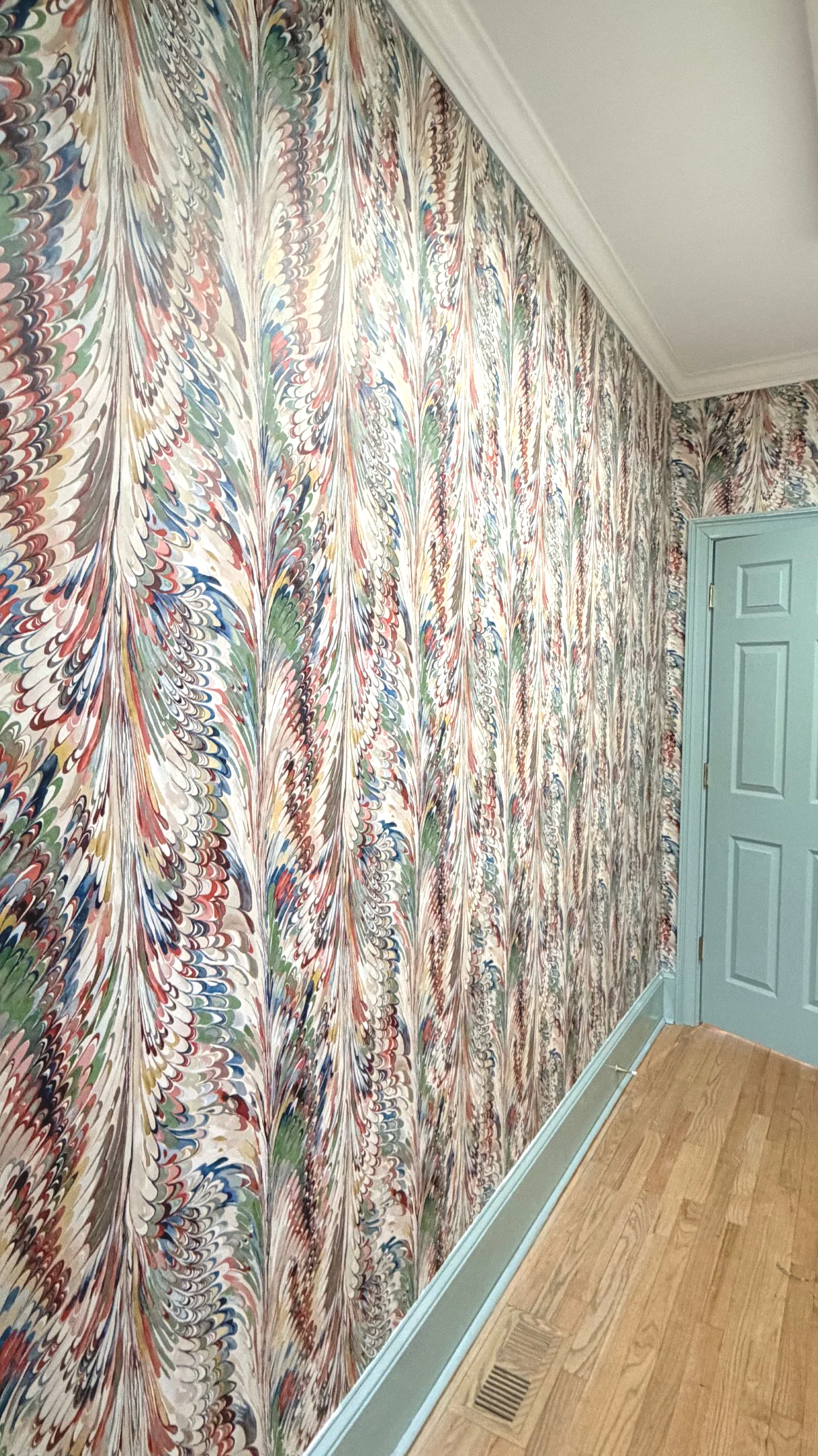 A wall covered with colorful marbled wallpaper next to a light blue door and a hardwood floor.