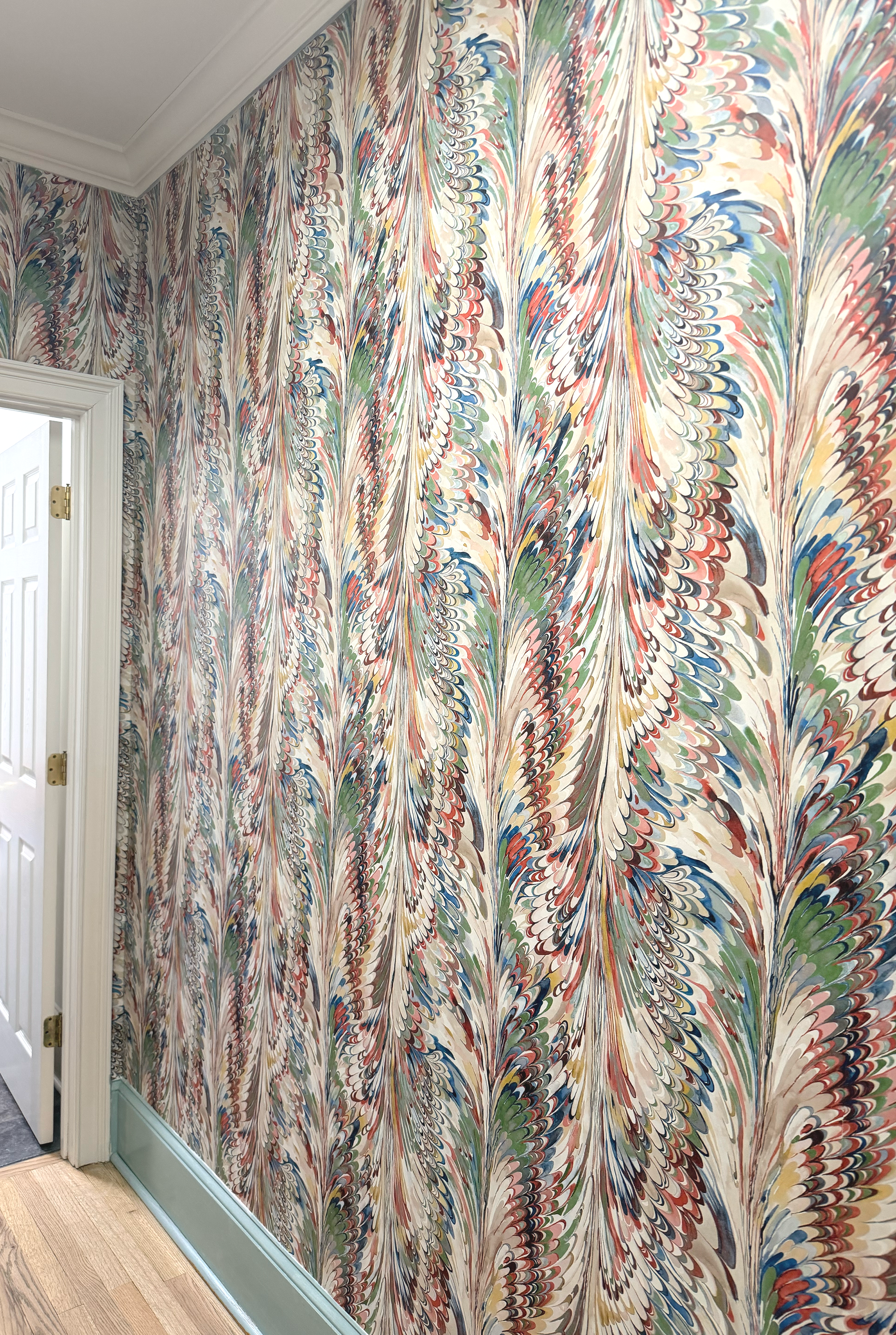 Colorful marbled wallpaper with red, blue, green, yellow, and beige swirls covering an interior wall near a door with white trim and a wood floor.