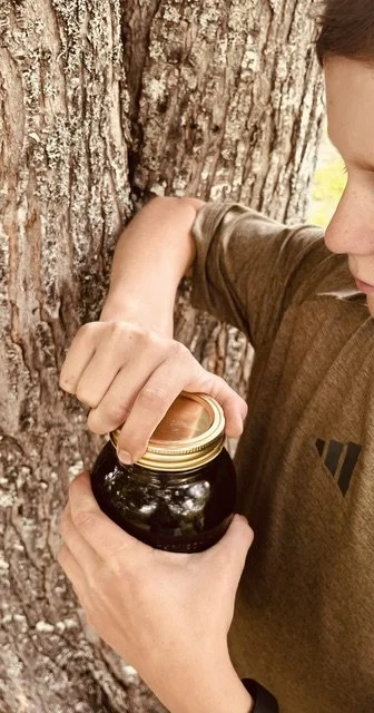 Person opening a jar of blackberries or jam next to a tree.