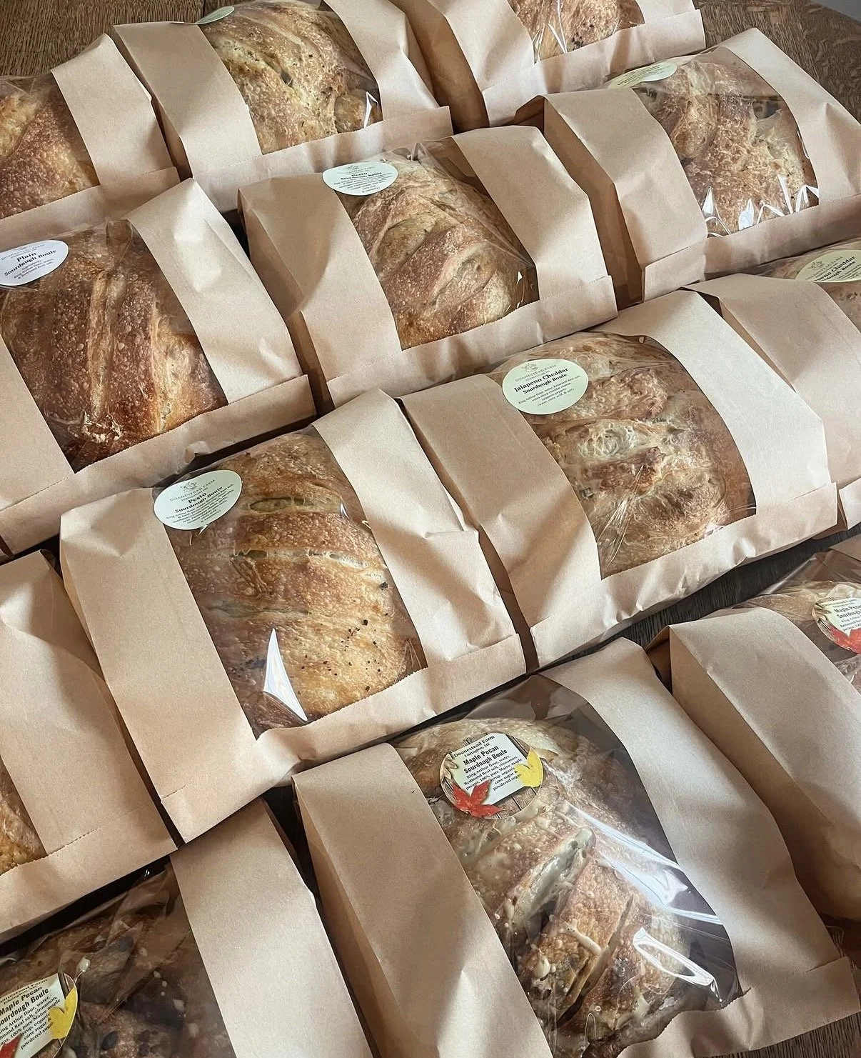 Multiple loaves of bread in paper bags with clear windows, arranged on a surface.
