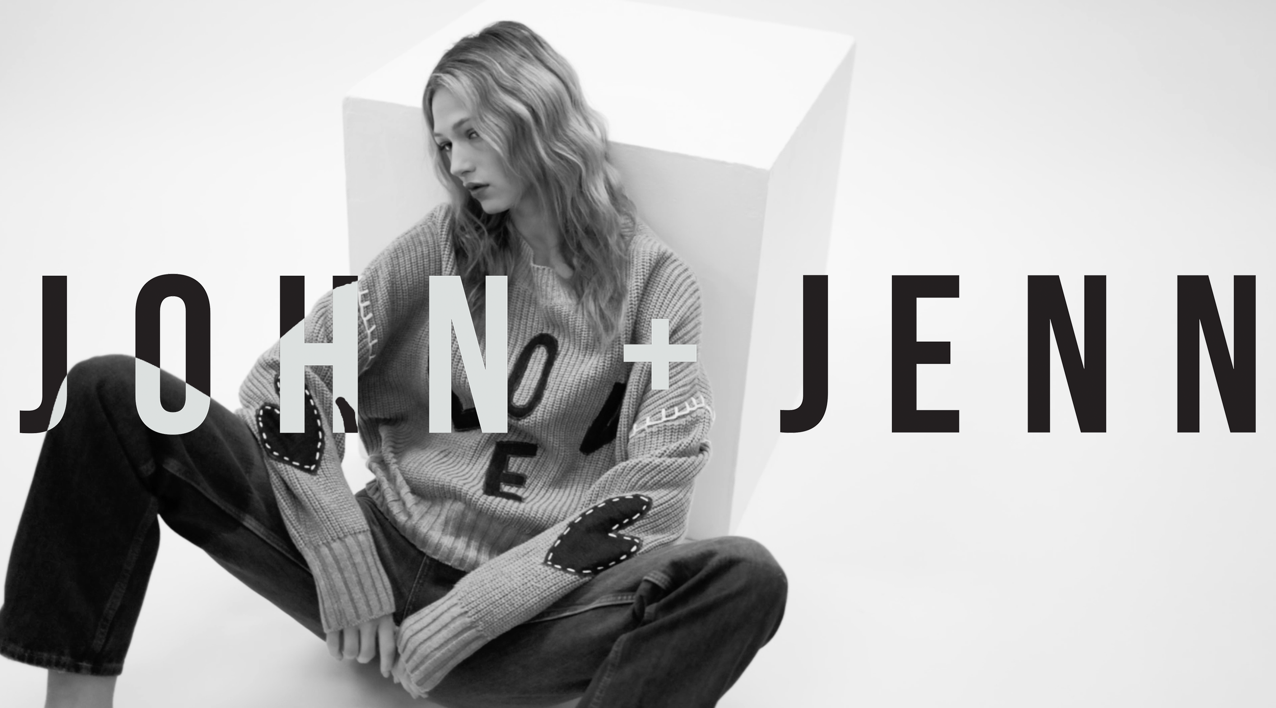 Black and white photo of a young woman with wavy hair, sitting against a white background with a large white geometric shape behind her. She is wearing a sweater with letters and patterns, dark jeans, and a glove. The text 'JON + JENNY' is overlaid on the image.