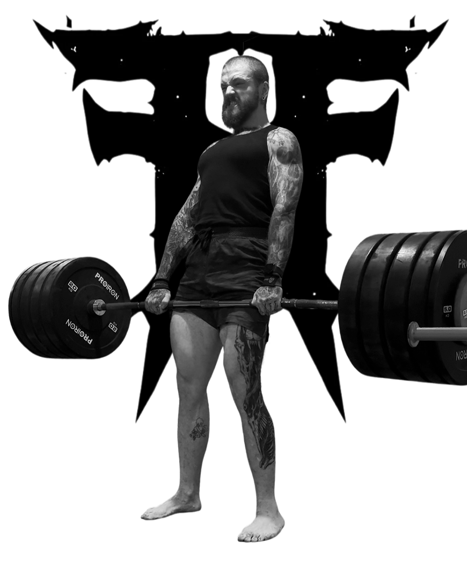A muscular man with tattoos on his arms and legs, beard, and short hair, lifting a loaded barbell with multiple weights in a gym or fitness setting, posing in front of a black backdrop with a stylized dragon or bat design.