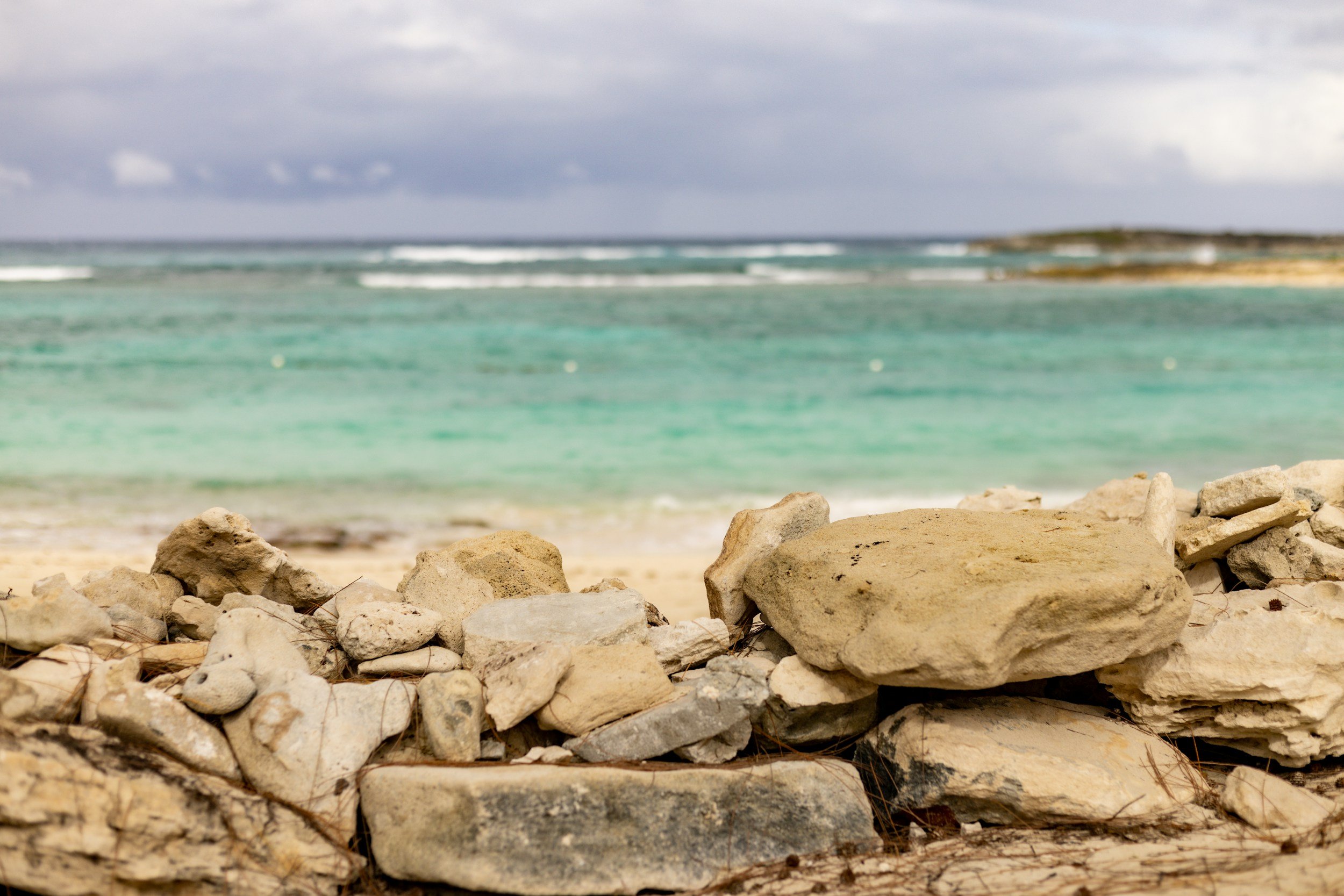 Rocky beach in the foreground with a calm ocean and cloudy sky in the background.
