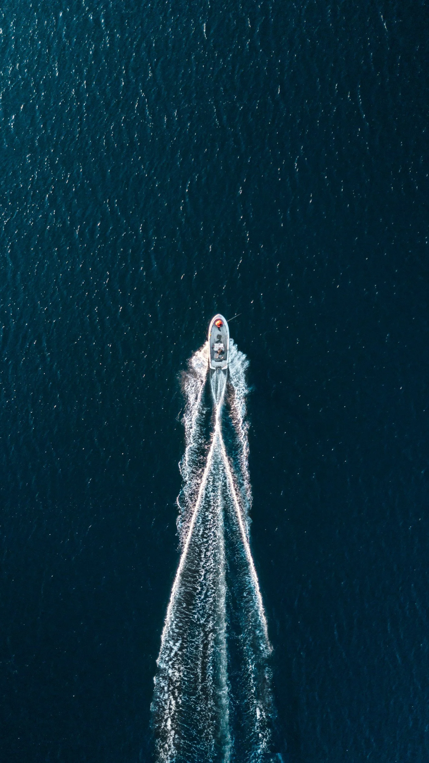 An aerial view of a boat sailing on the ocean, creating a wake behind it.