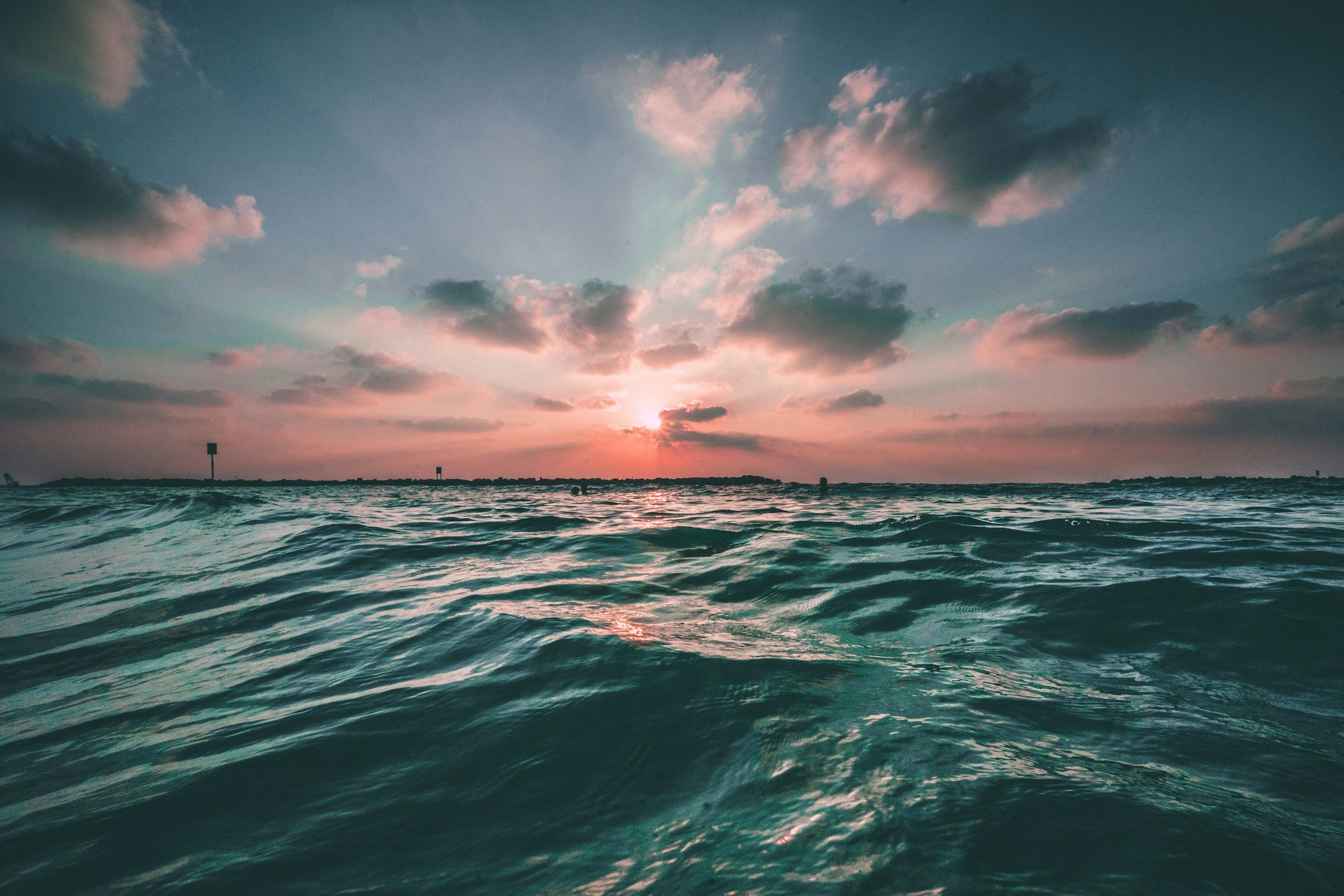 Sunrise or sunset over the ocean with a few clouds in the sky and water with small waves.