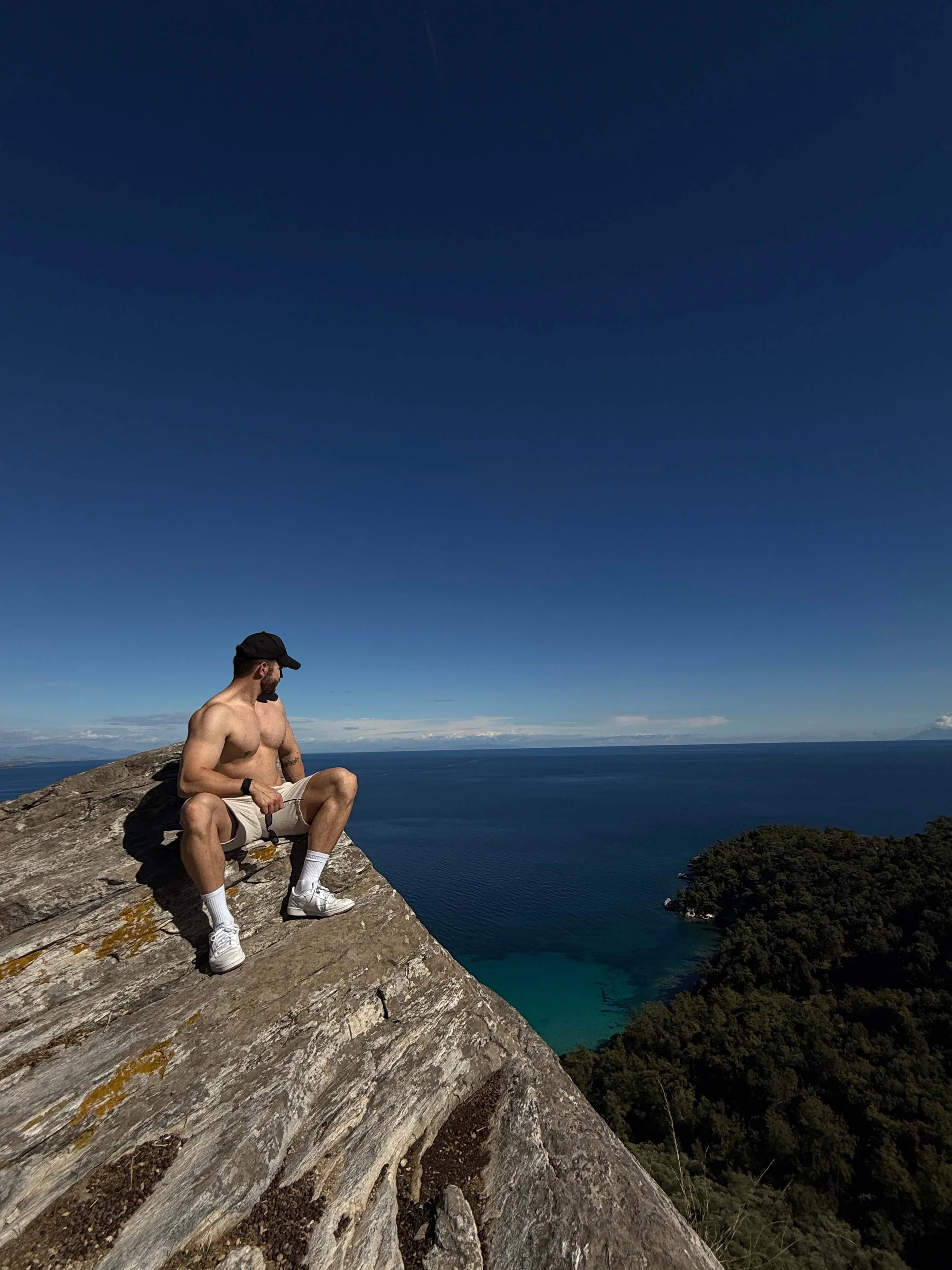 Ein athletischer Mann sitzt auf einem Felsen und genießt die schöne Aussicht auf das blaue Mittelmeer.