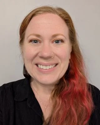 A woman with red hair and a nose piercing smiling at the camera.