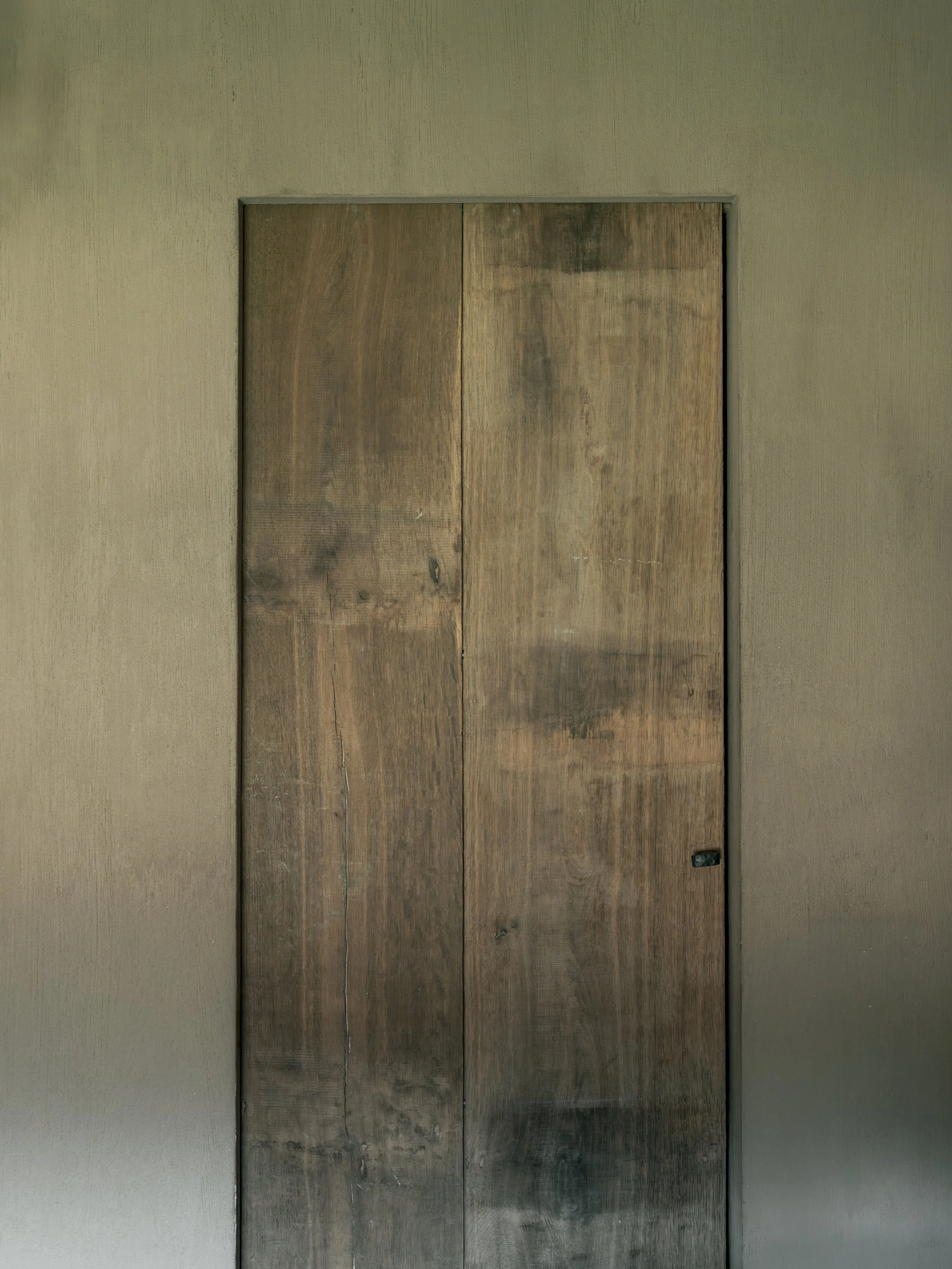 A wooden door with visible grain, knots, and weathered surface set in a beige wall.