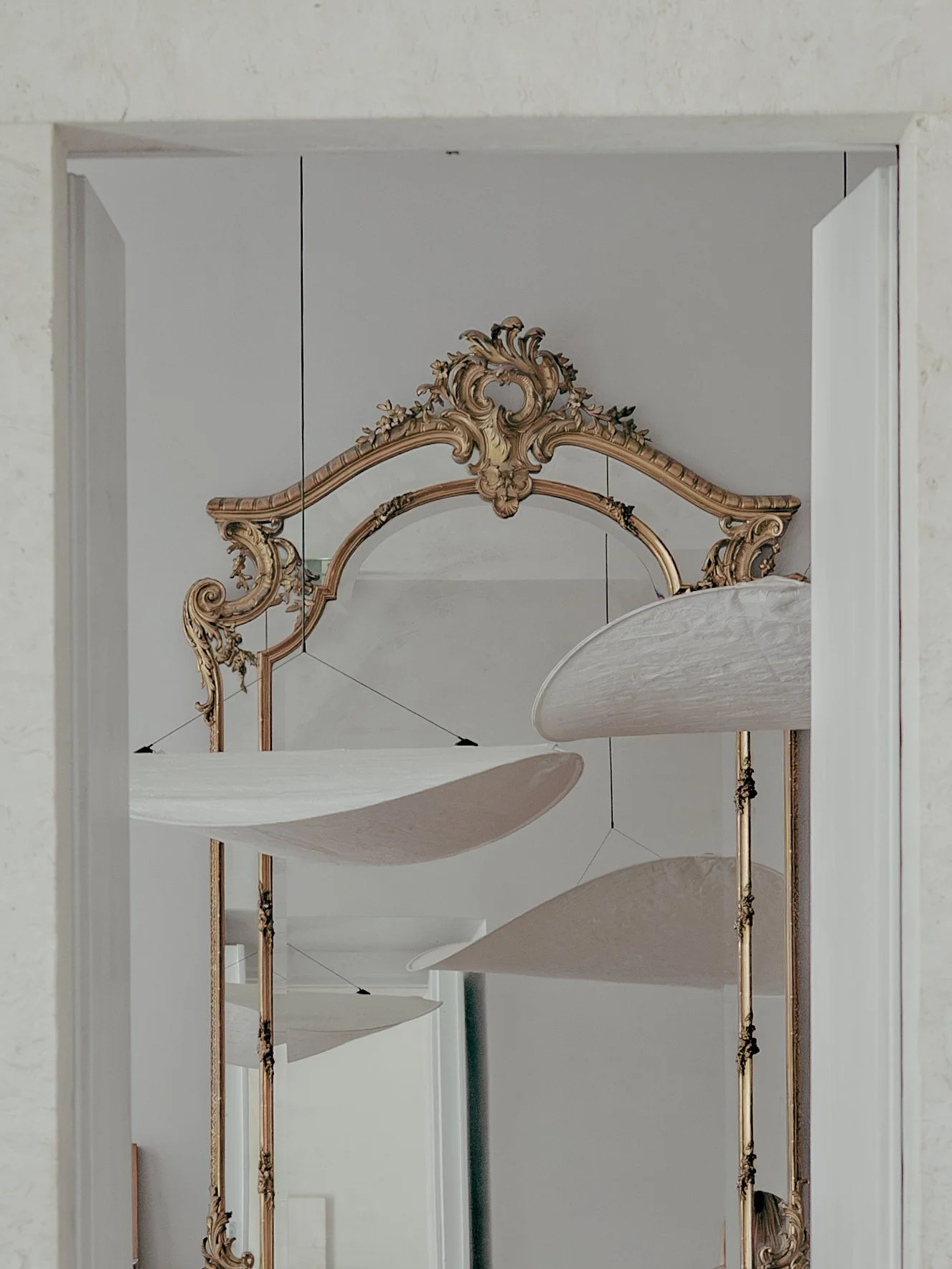 Decorative mirror with an ornate gold frame hanging on a wall, and a series of descending curved architectural details or panels, reflected in the mirror.