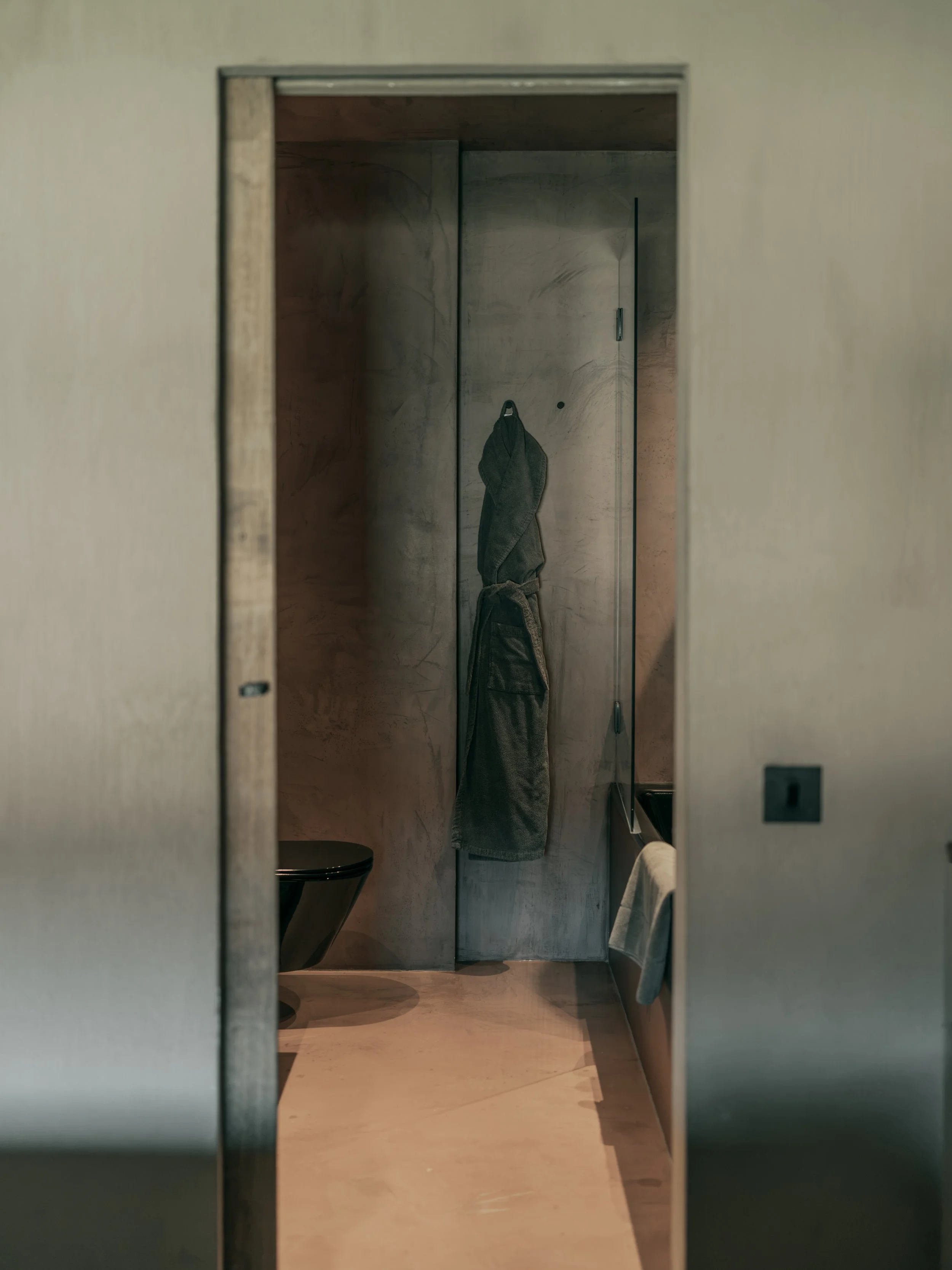 A bathroom with a mirror, a black toilet, and a towel hanging on the wall.