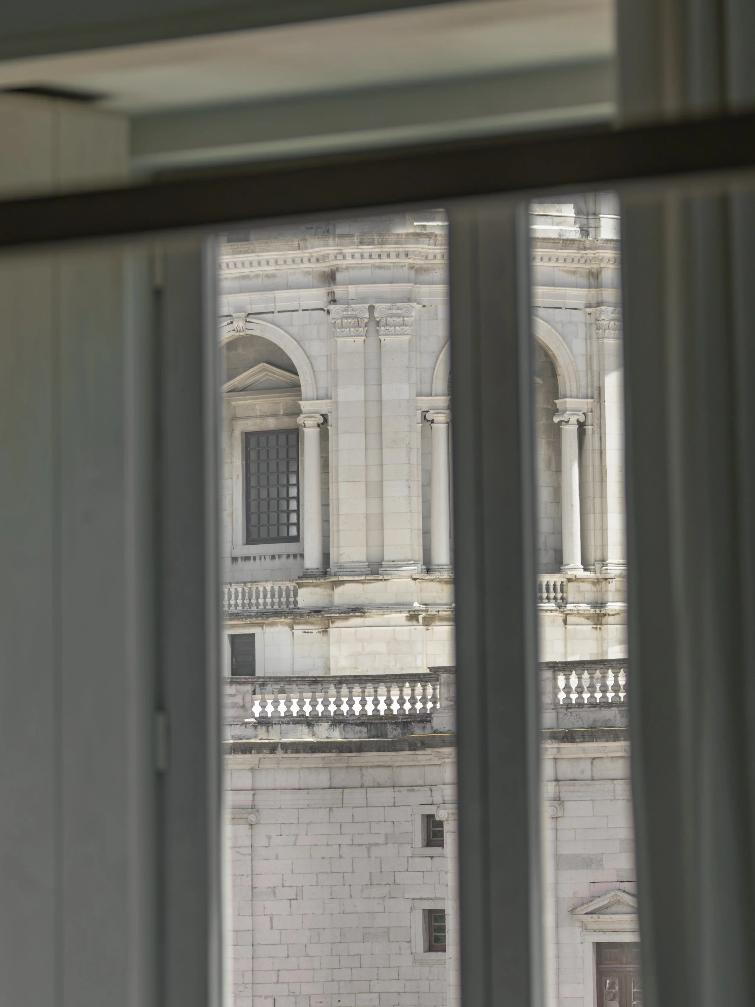 View of a historic building through window bars, showing classical architecture with columns, arches, and ornate details.