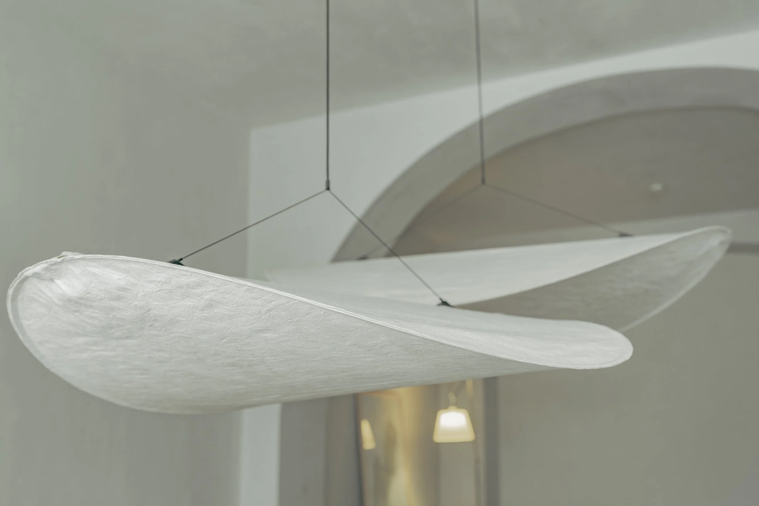 Close-up of a modern ceiling light fixture with a paper or fabric shade, suspended from the ceiling with thin wires.