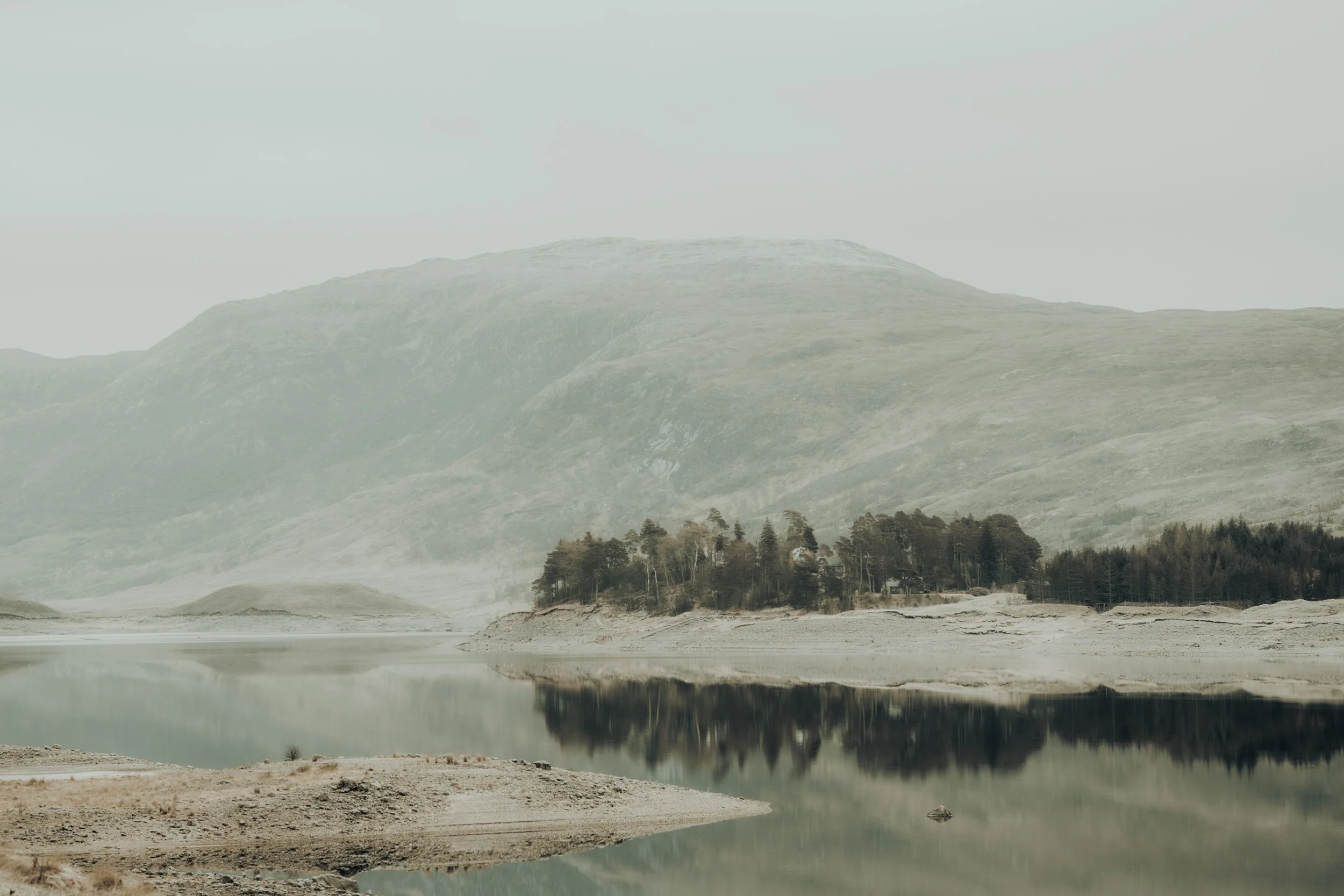 Scotland highland loch with mountain, trees, water and mist at dawn. Loch Cluanie.