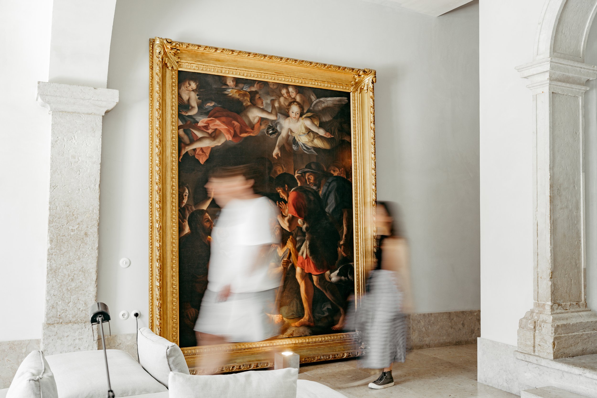 Large framed classical painting on a wall in an art gallery or museum with visitors viewing the artwork.