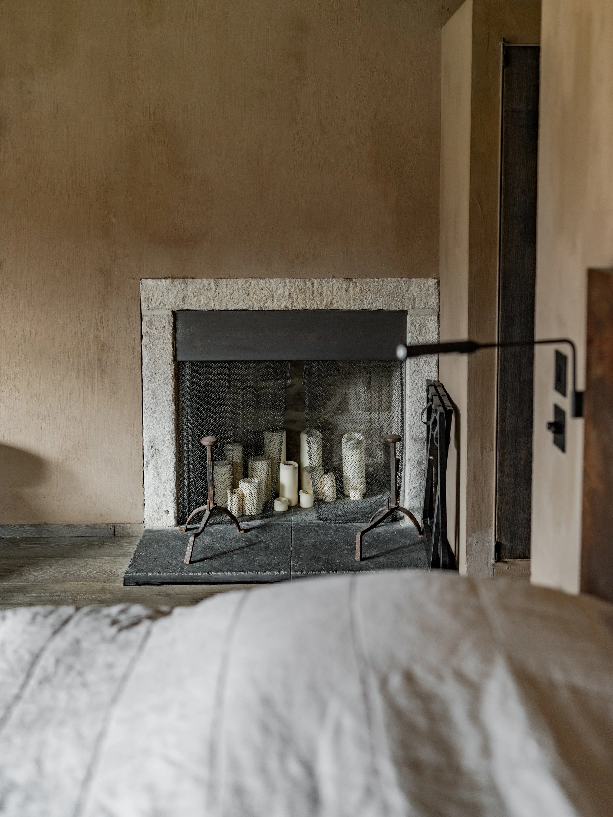 Living room fireplace with candles inside, beige walls, and a partial view of a beige armchair in the foreground.