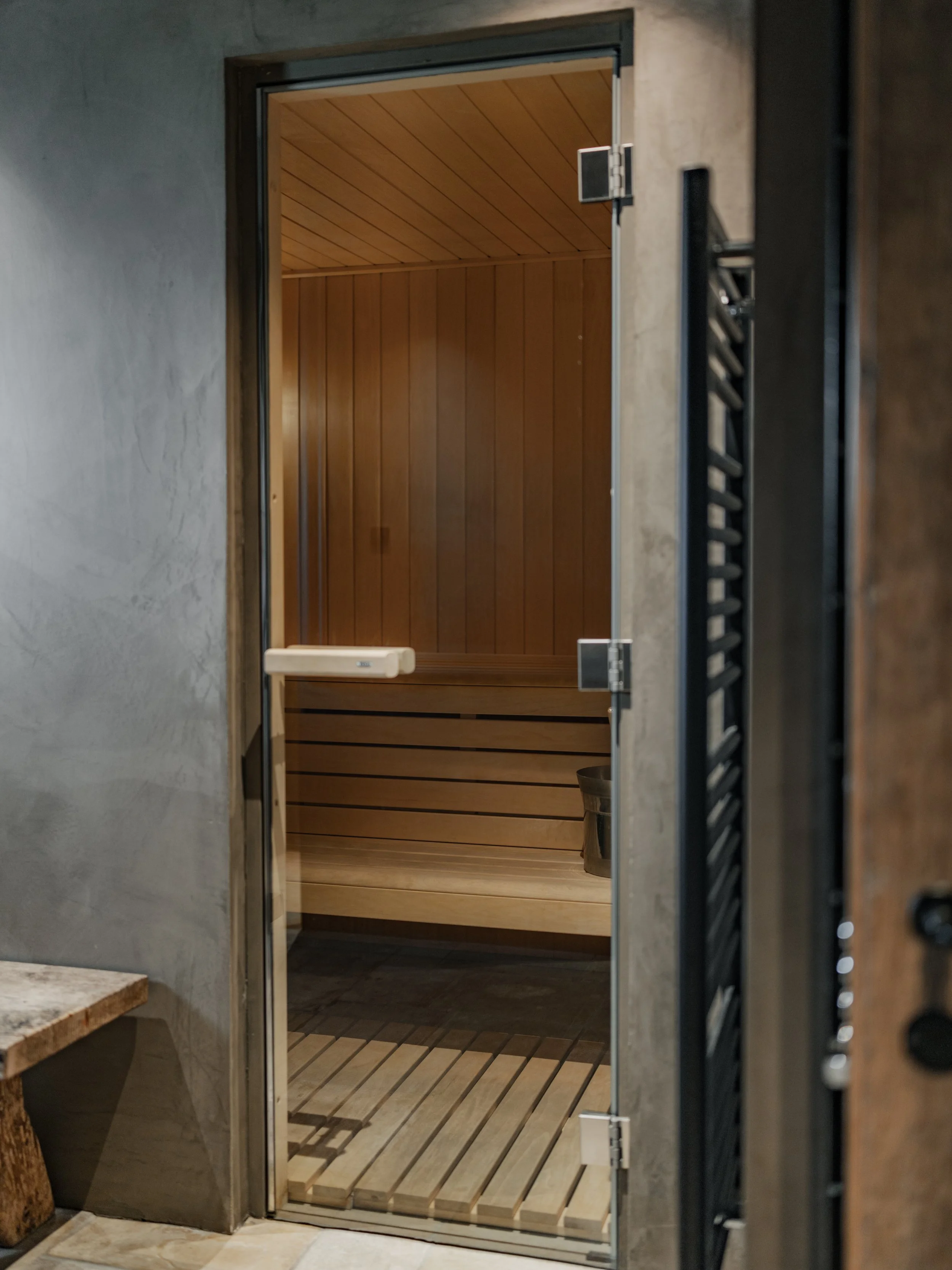 Interior view of a sauna with wooden walls, ceiling, and floor slats, visible through a glass door.