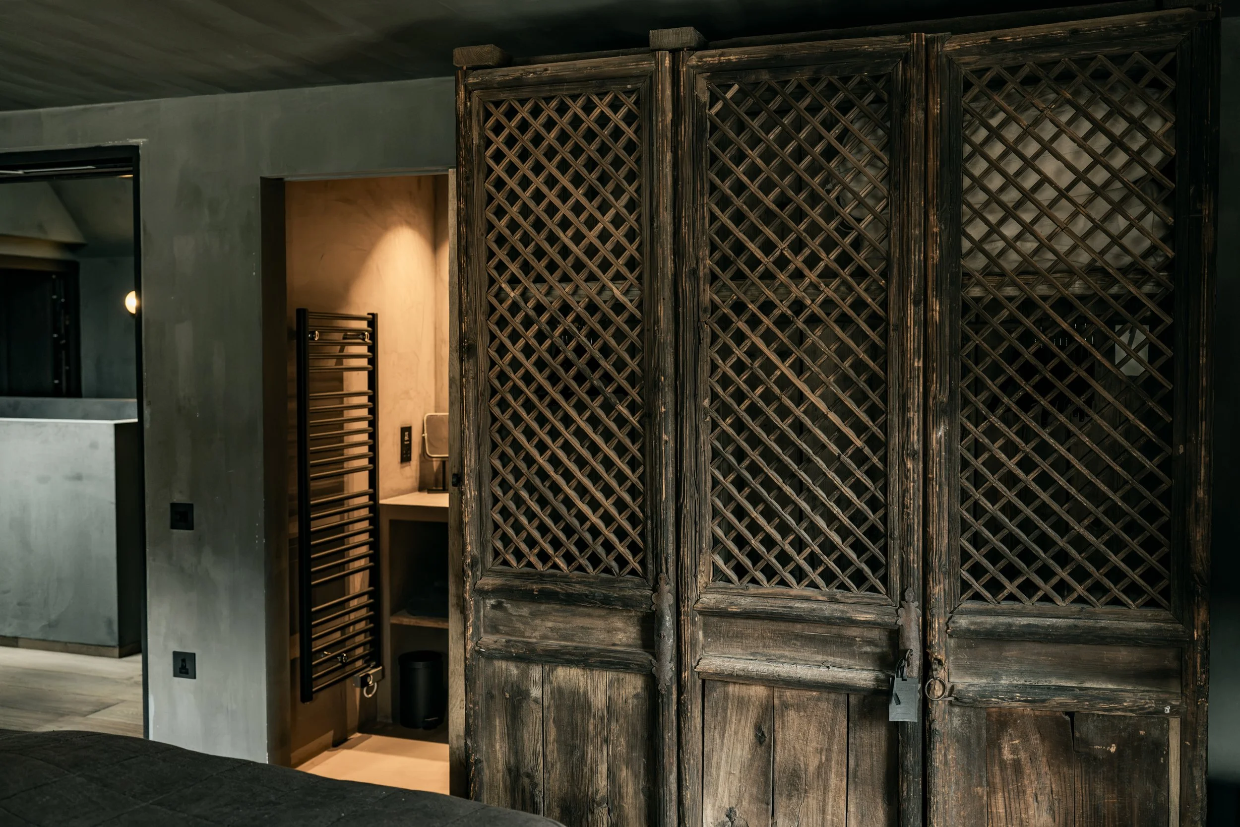 An interior space featuring a large, rustic wooden folding screen with a lattice design, a bathroom sink with a mirror, and a black towel warmer on the wall.