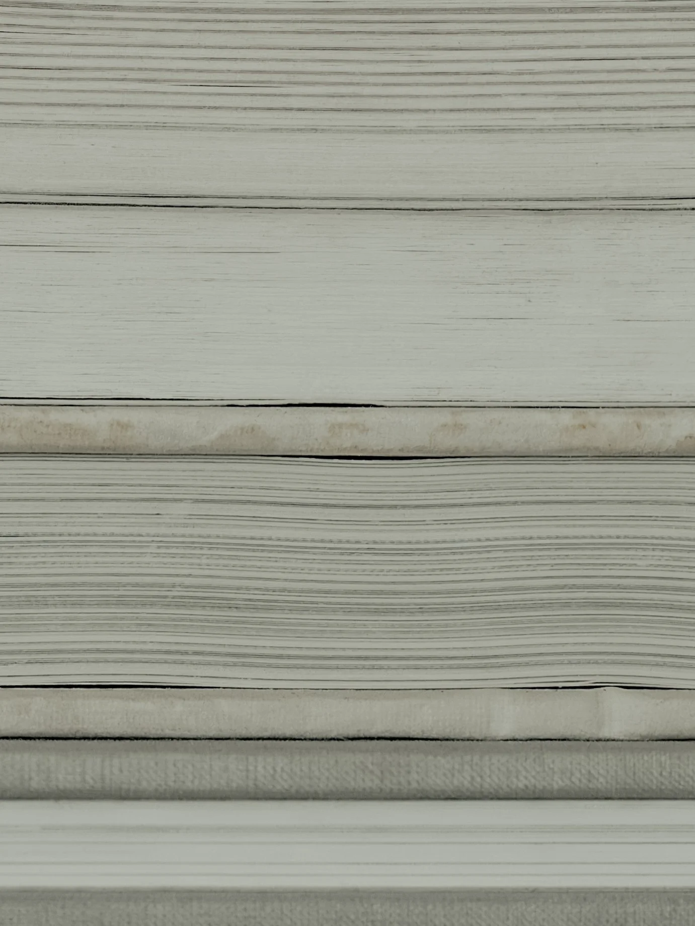 Close-up of a thick stack of books lined up horizontally, showing their spines on a white surface.