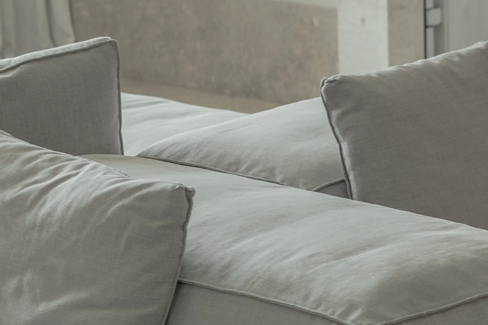 Close-up of a bed with beige or light gray pillows and bedding in a neutral-toned room.