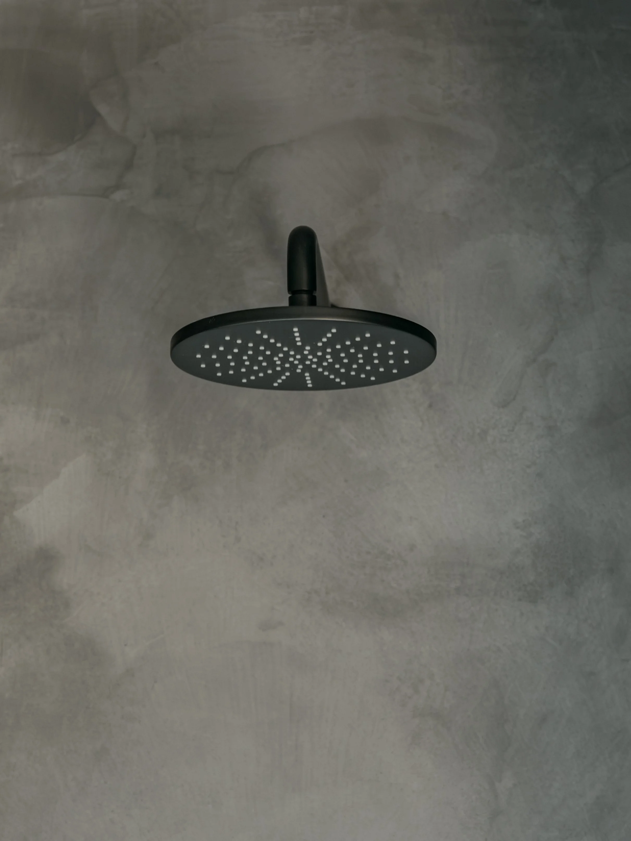 A black shower head mounted on a gray concrete ceiling.