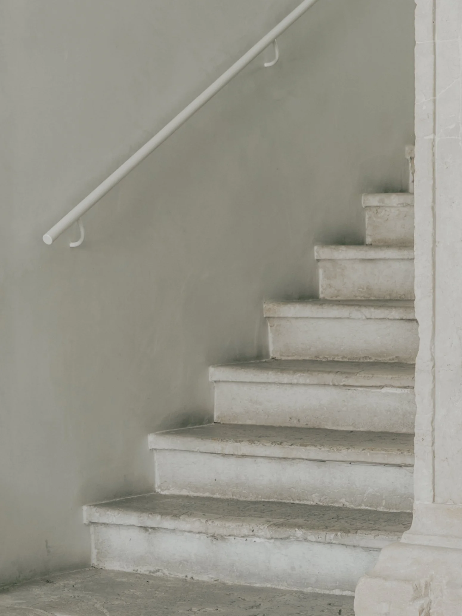 Concrete stairs with a white handrail on a gray wall.