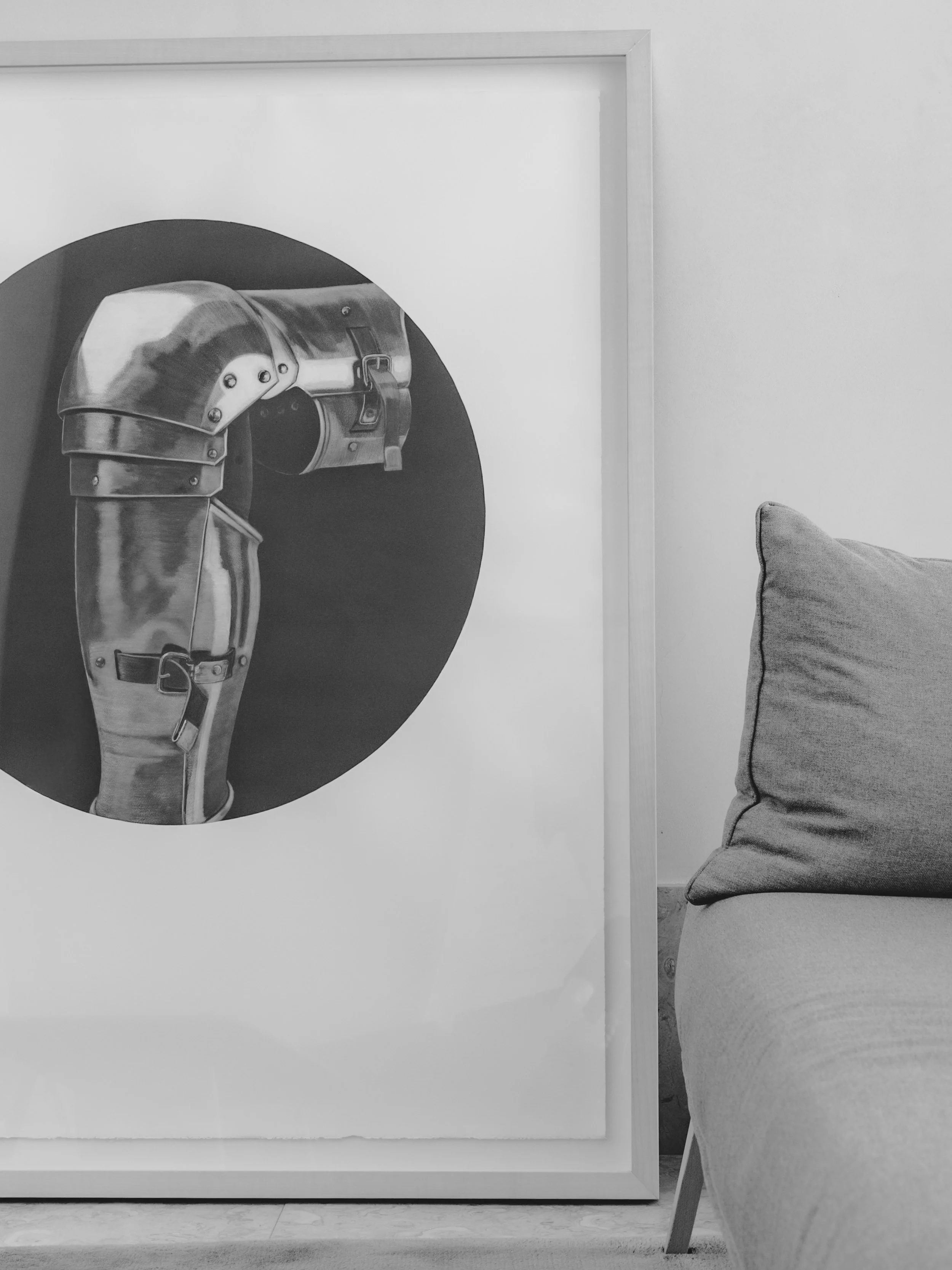 Black and white photo of a modern styled room with a large painting of a mechanical robotic arm on the wall and a light-colored upholstered armchair nearby.