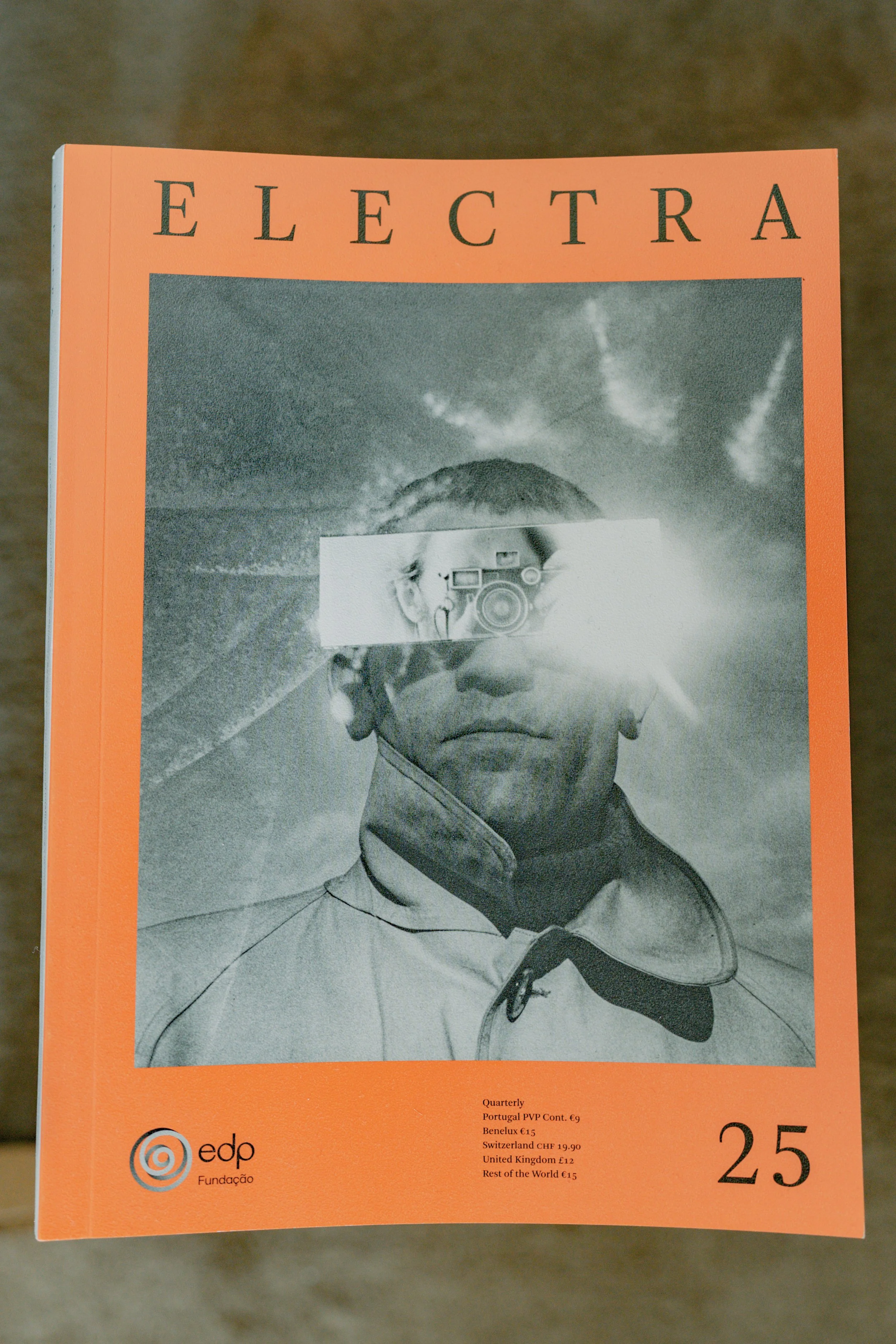 A magazine or publication cover featuring a grayscale portrait of a young man with a serious expression, wearing a collared shirt, with a camera obscuring part of his face. The cover has an orange border, and the title "ELECTRA" at the top. There is 