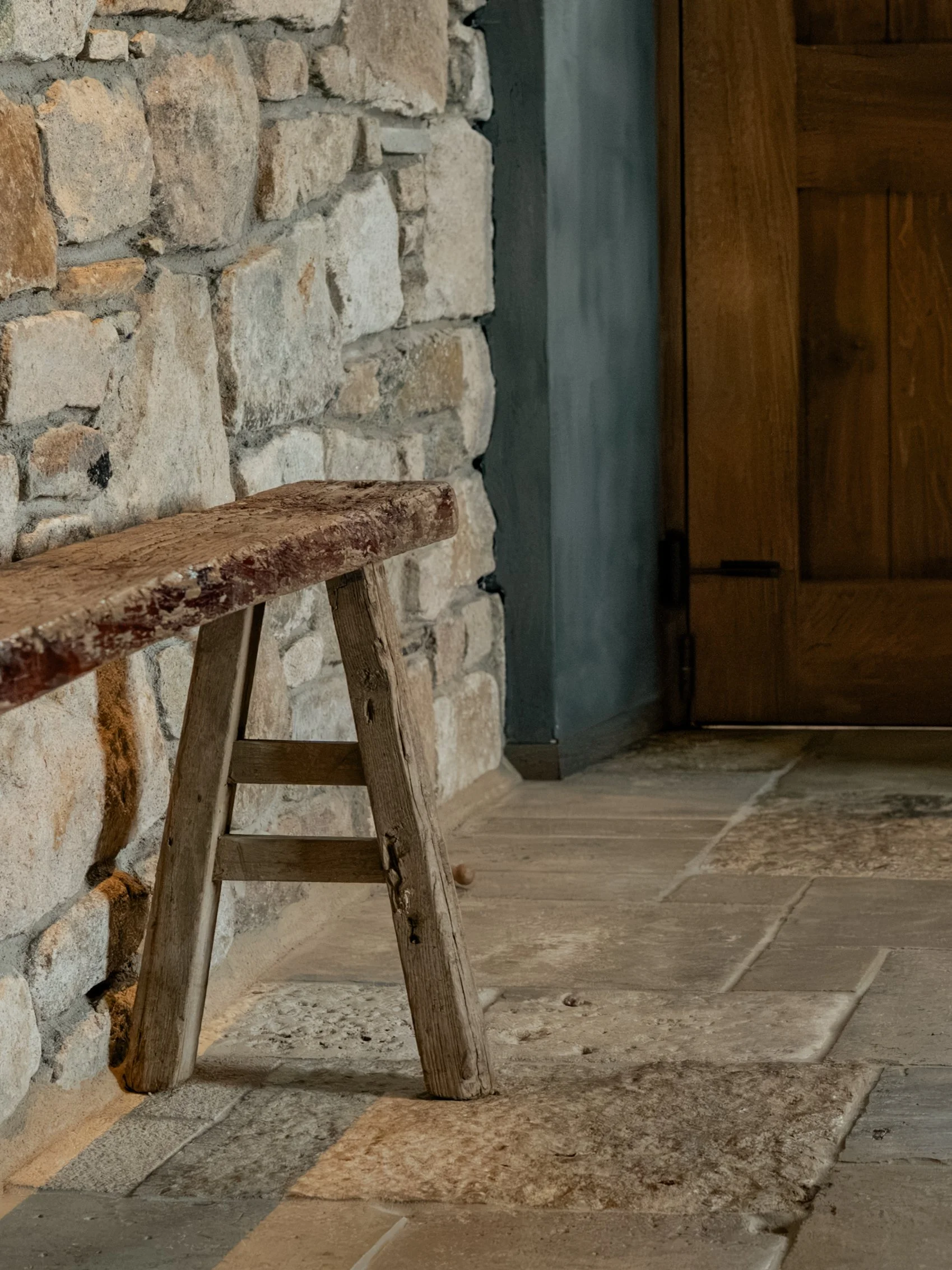 A rustic wooden ladder leaning against a stone wall with a wooden door nearby.