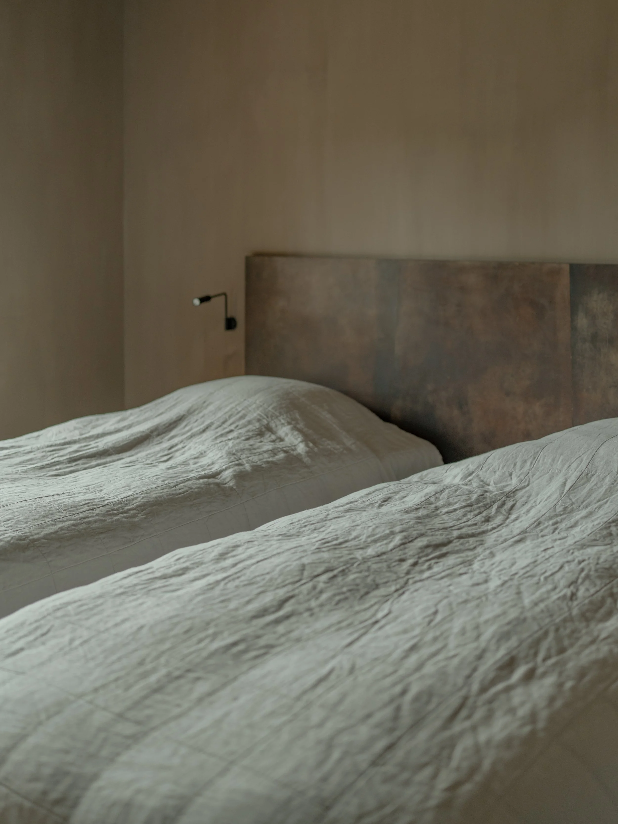 Photo of a bed with beige linen sheets and a wooden headboard in a minimalistic bedroom.