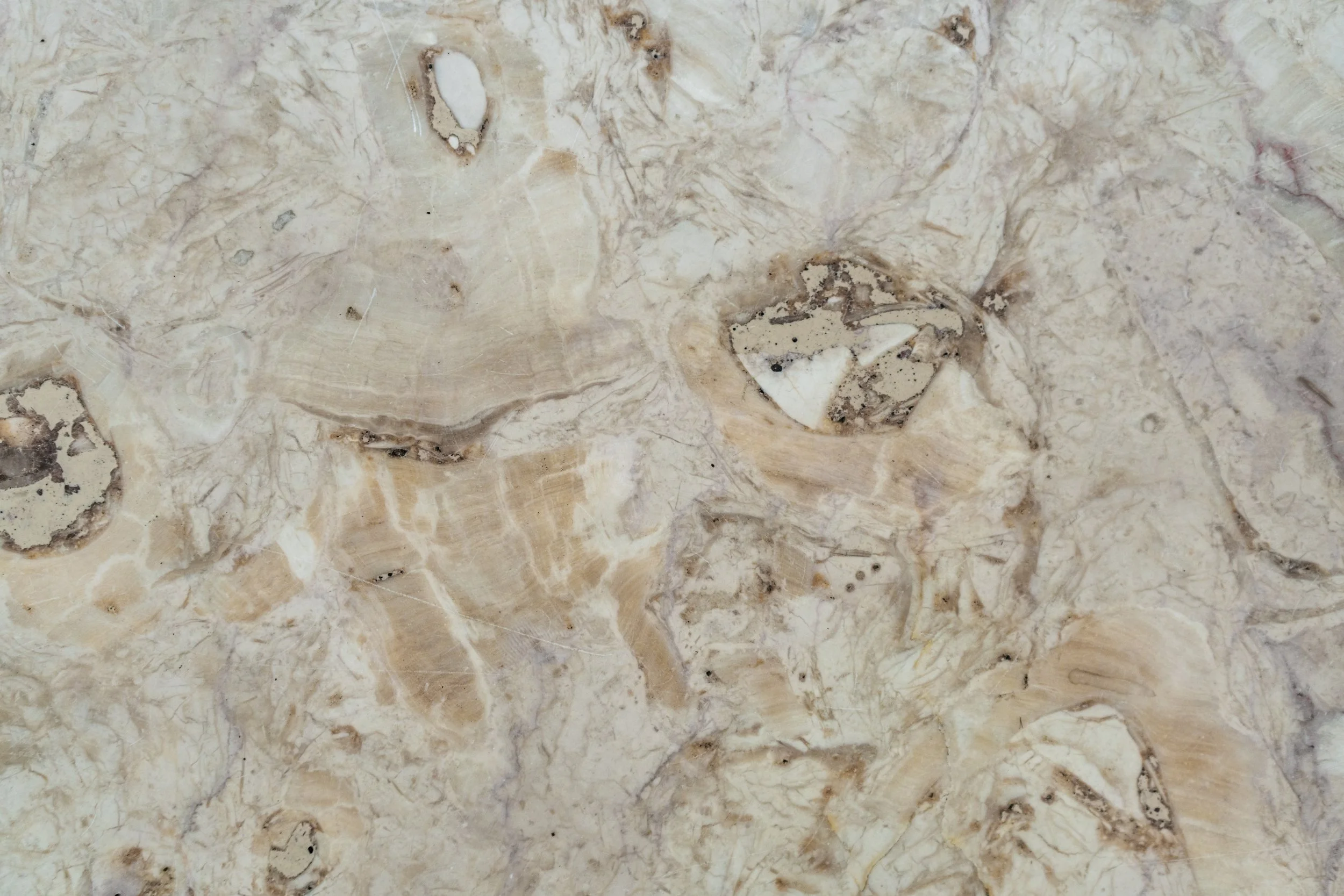 Close-up of a beige natural stone surface with various swirls, veins, and small mineral inclusions.