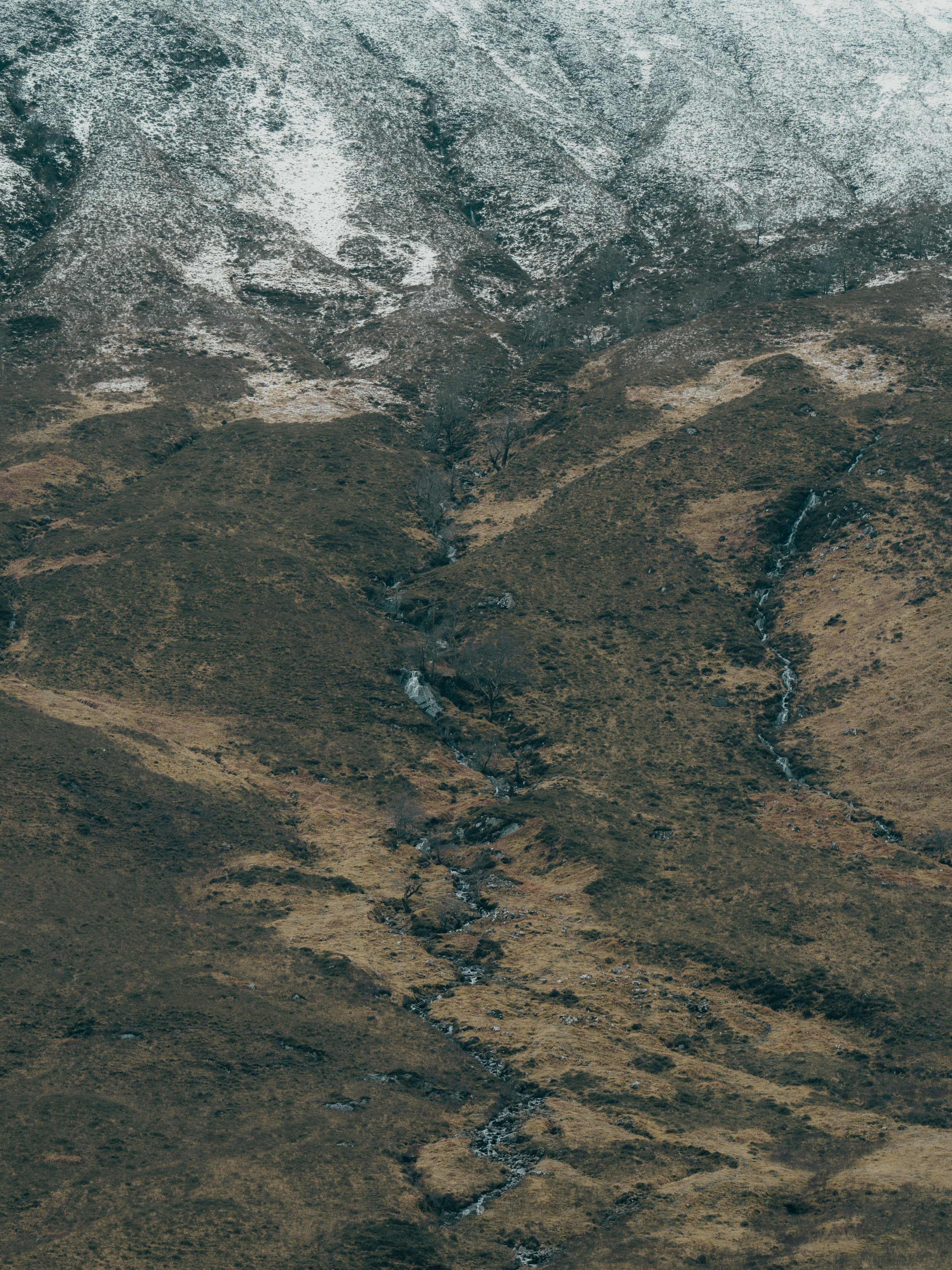 A mountainous landscape with patches of snow on the peaks and small streams flowing down the slopes.