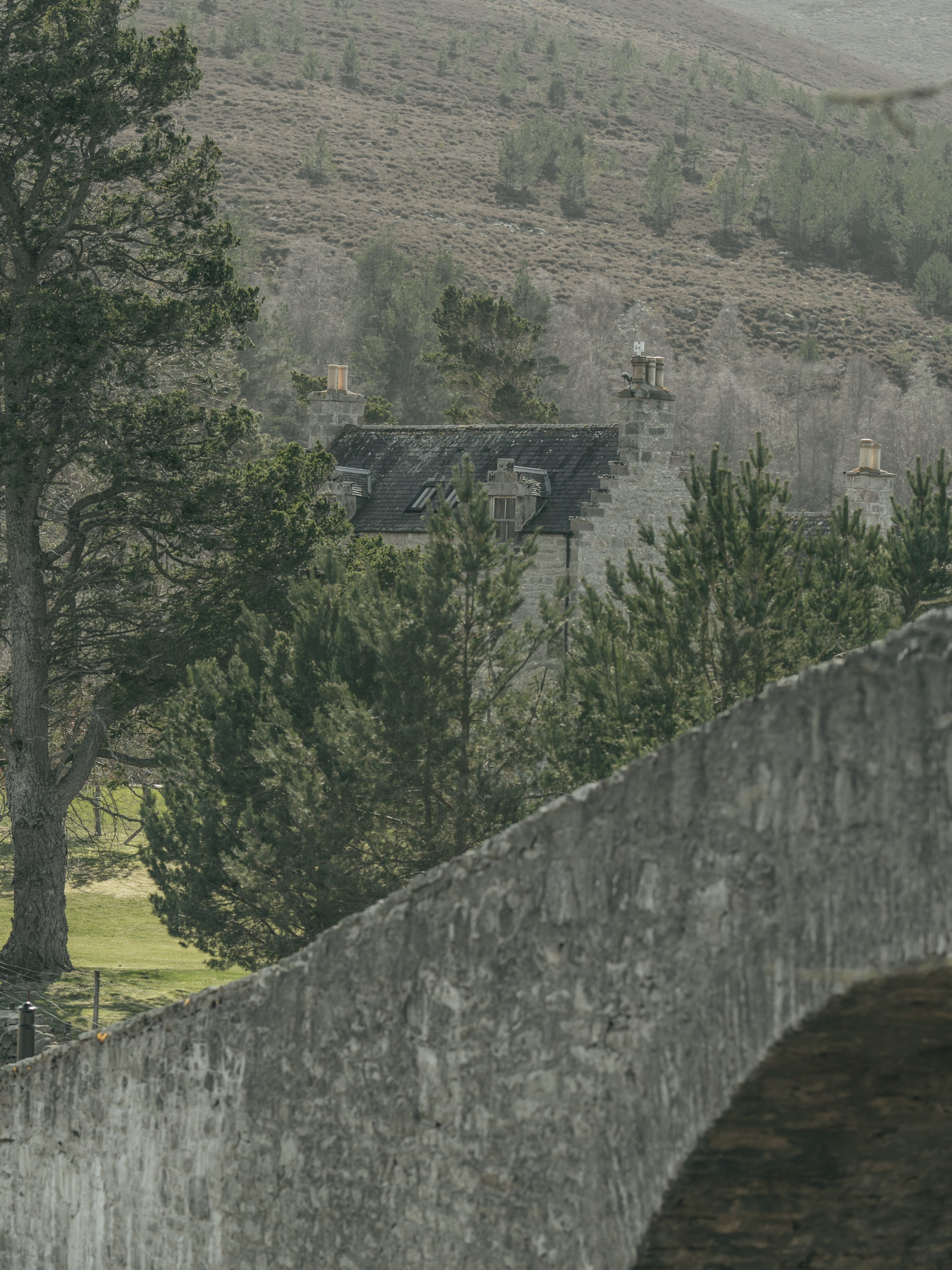 A stone bridge over a body of water with trees and hills in the background.