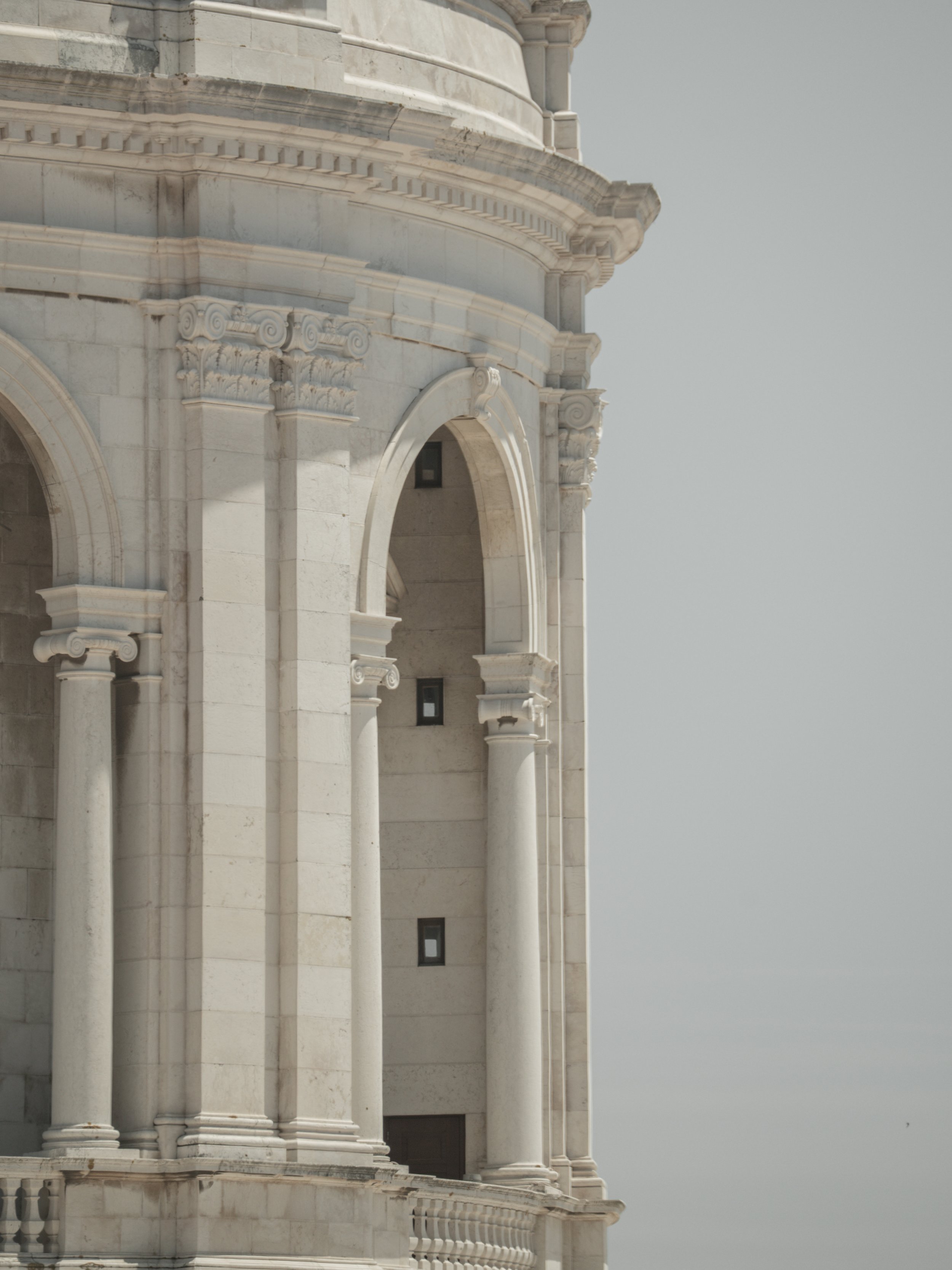 Close-up of a detailed white marble building with classical architectural features, including columns, arches, and ornate capitals, against a gray sky.