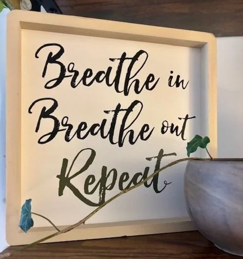 Framed artwork on a desk with text Breathe, in Breathe Out, Repeat with a piece of vine houseplant draped in front.