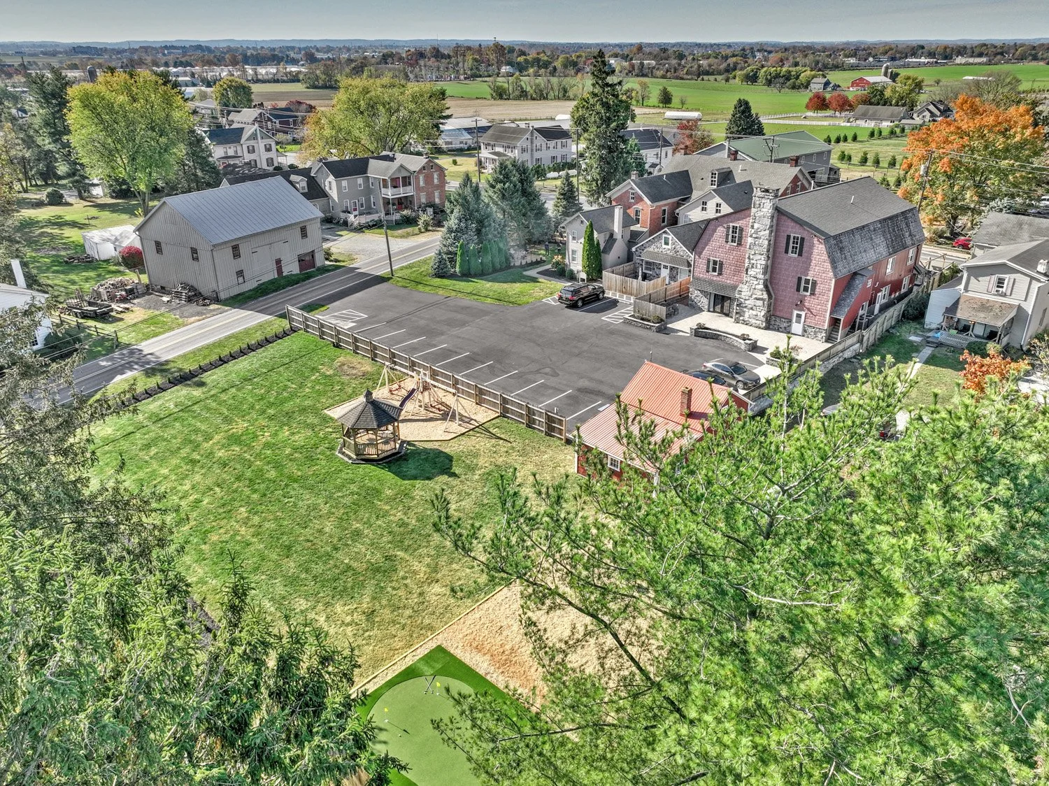Aerial view of a suburban neighborhood with houses, a parking lot, a playground, and green fields with trees.