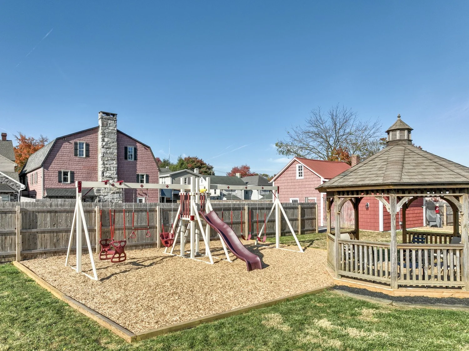 Backyard playground with a swing set, slide, and a small gazebo on a sunny day.