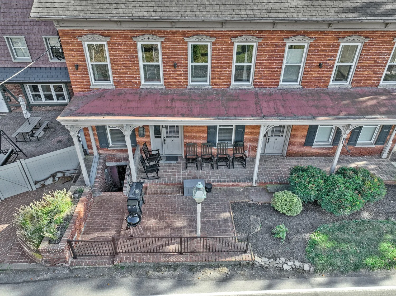 An aerial view of a brick building with a porch, chairs, and greenery.
