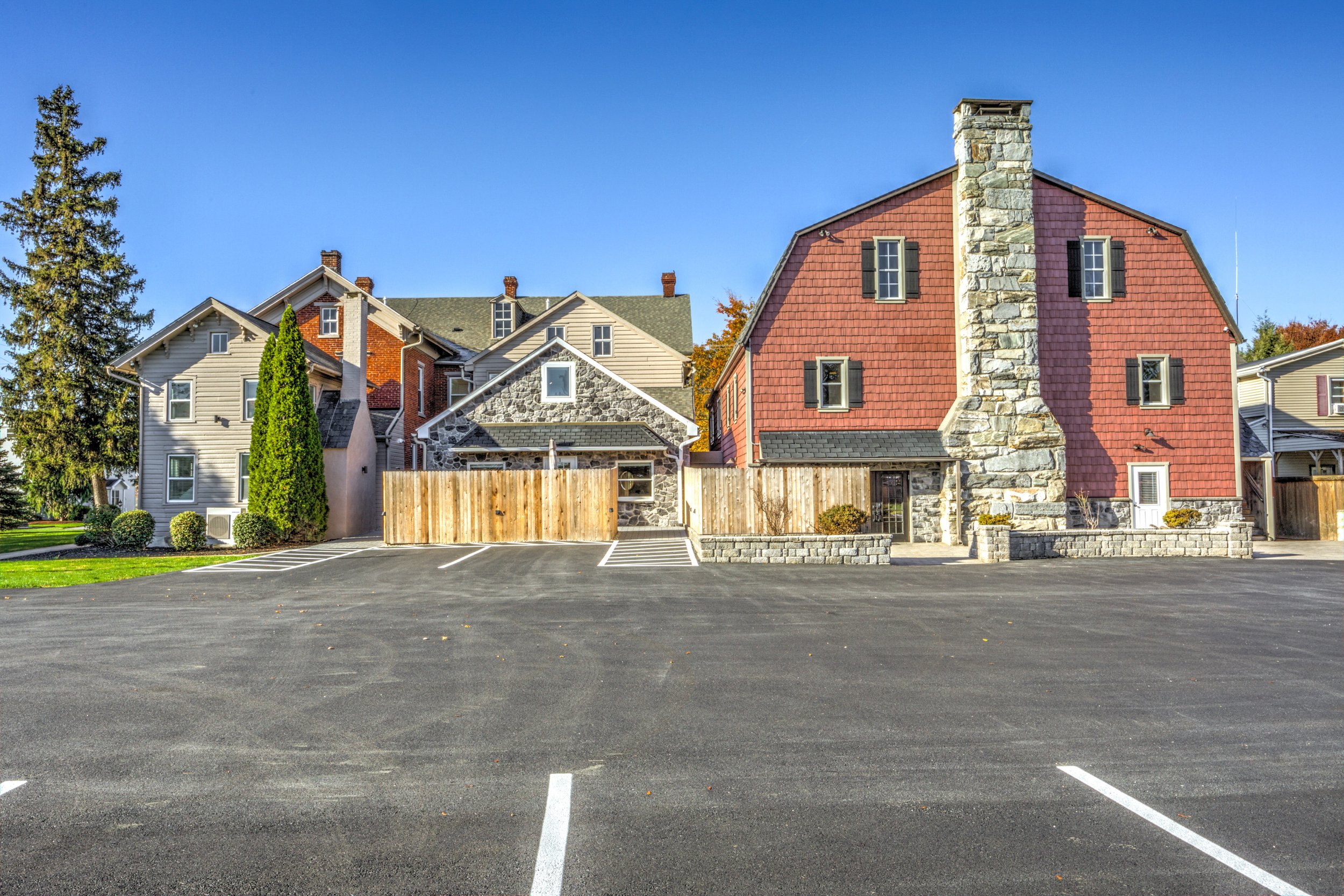 Empty parking lot in front of residential houses with trees and a clear blue sky.