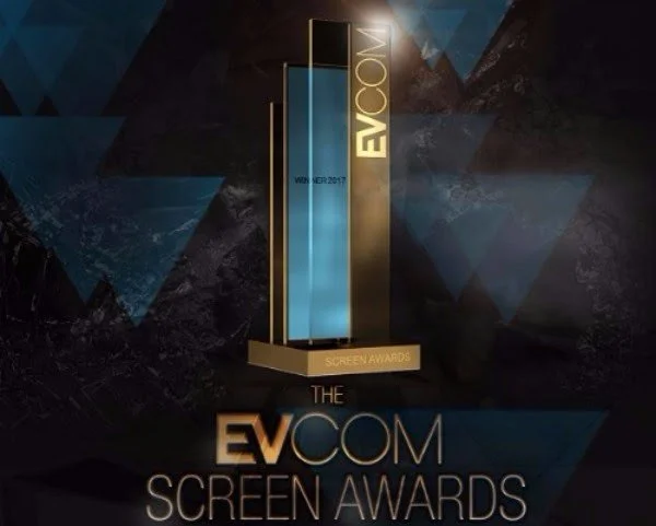 An award trophy for the EVCOM Screen Awards with a tall, modern design in front of a dark, geometric background.