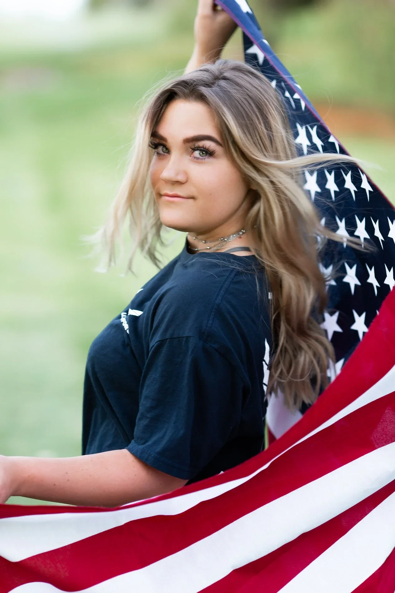 Young woman holding an American flag outdoors in a park.