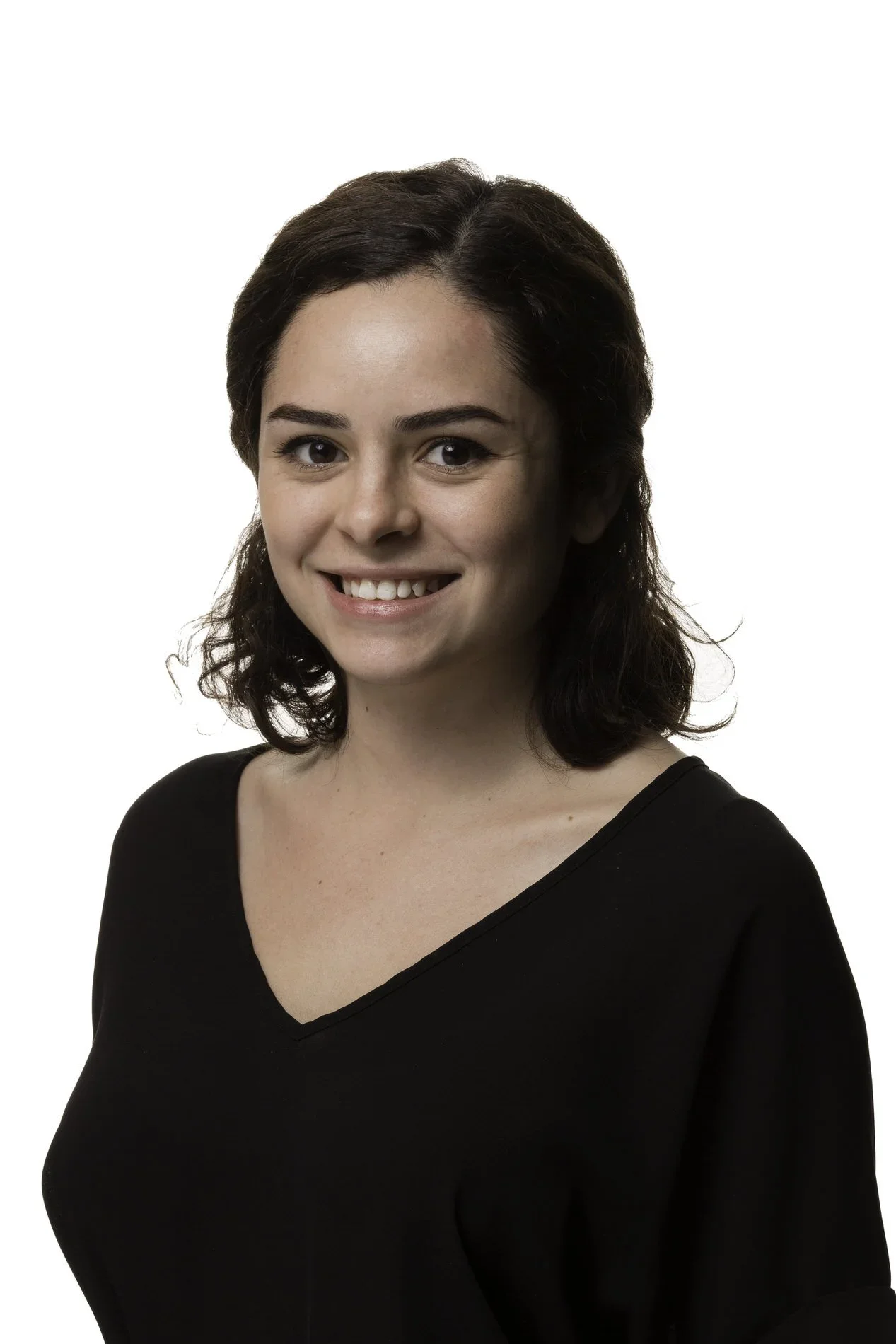A woman with shoulder-length dark brown hair, wearing a black V-neck top, smiling with white teeth, against a white background.