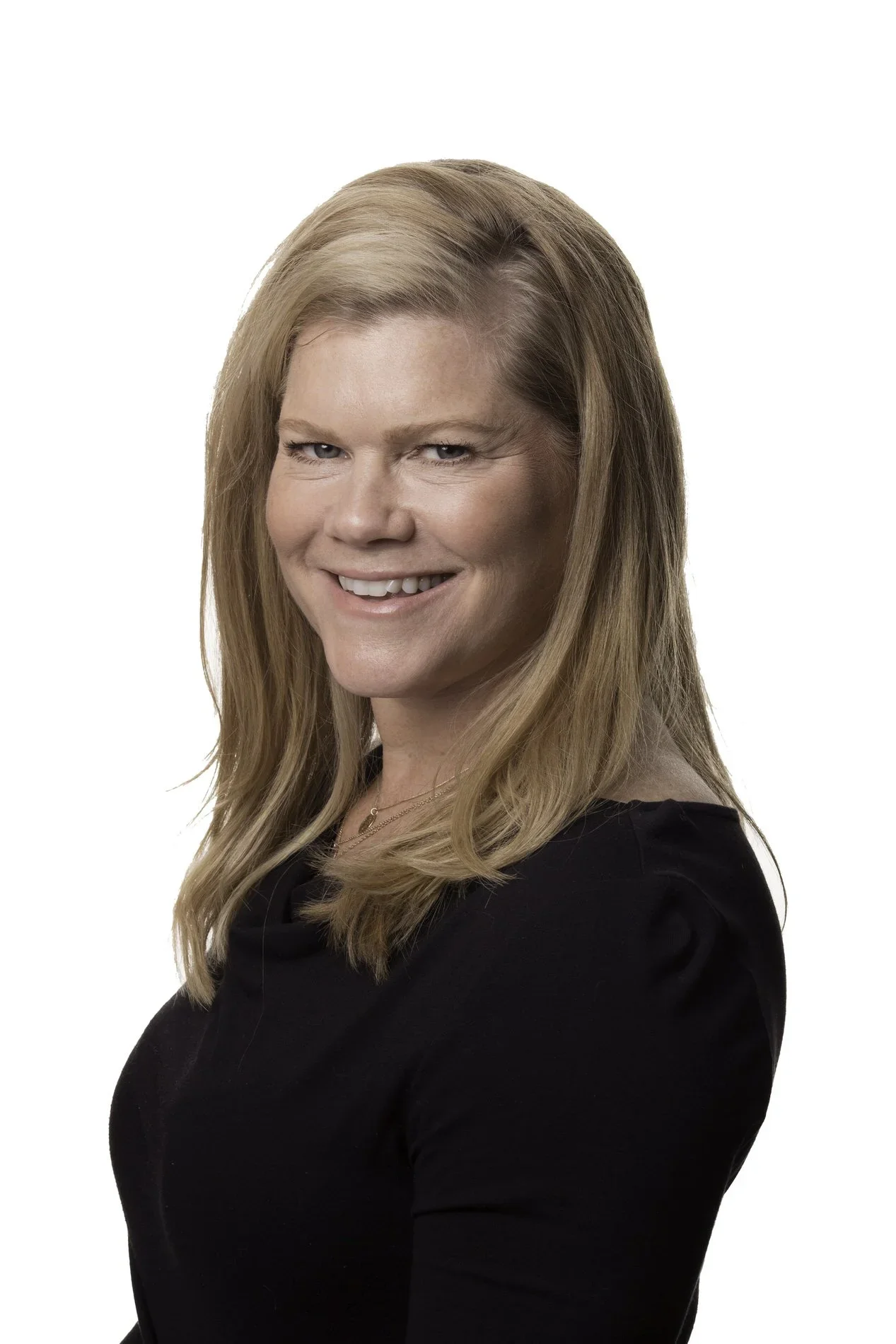 Portrait of a woman with long, blonde hair wearing a black top, looking at the camera and smiling against a white background.