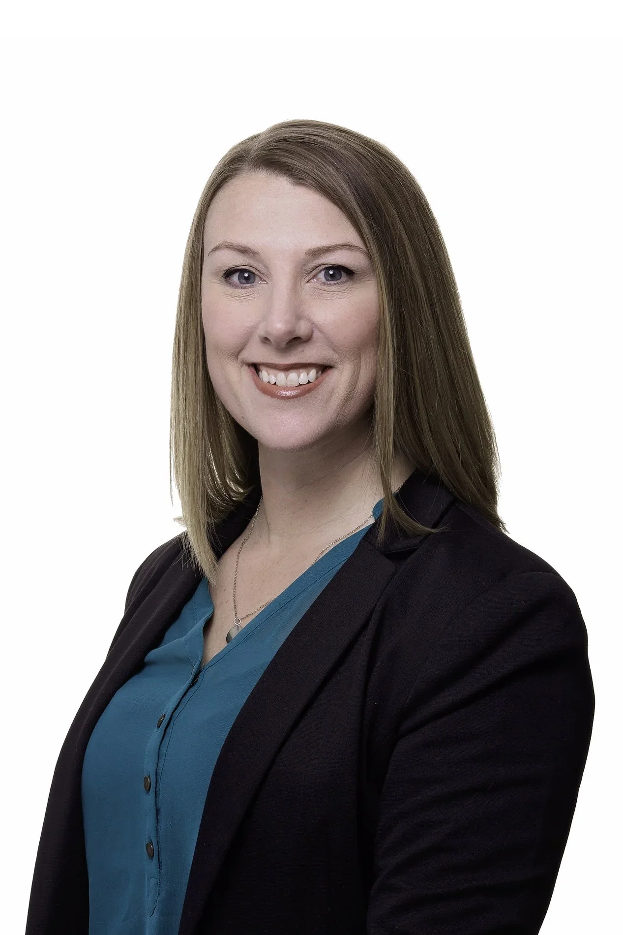 Professional woman with shoulder-length light brown hair, wearing a black blazer over a teal blouse, smiling in front of a white background.