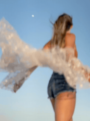 an animated image of julia at dusk, dancing in front of the moon. at first she's out of focus, and then she's in focus. she looks free, as her cardigan and hair flow wildly in the breeze