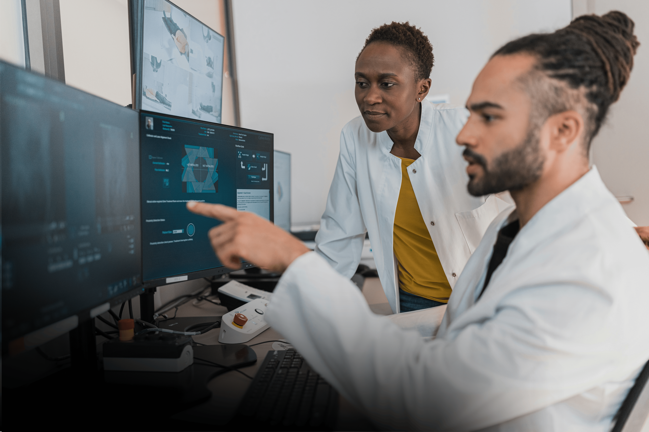 Two healthcare professionals in lab coats reviewing data on computer monitors in a medical office.