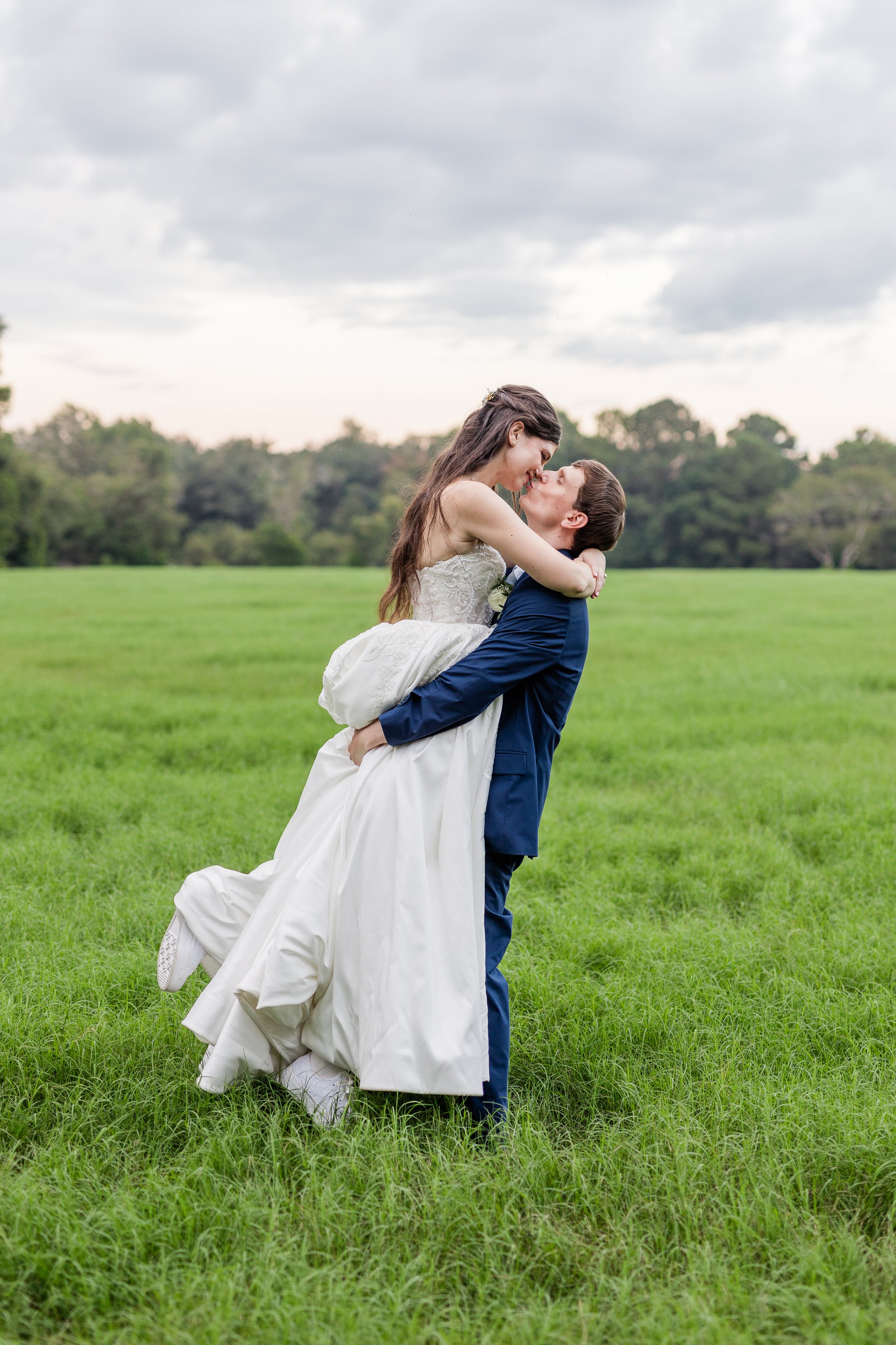 Groom lifting bride in a field, bridal hair and makeup by Briar & Bleu